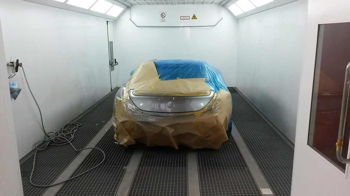 In einer Lackierkabine wird ein Auto mit Plastikfolie abgedeckt.