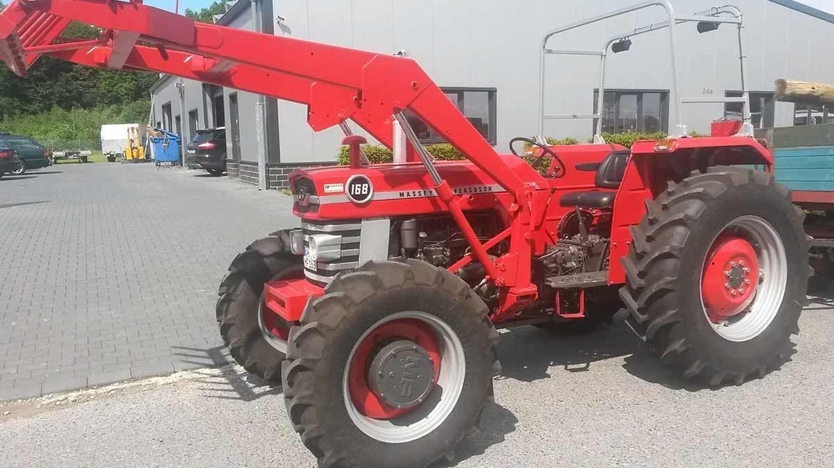 Ein roter Traktor steht auf einem Schotterplatz vor einem Gebäude.