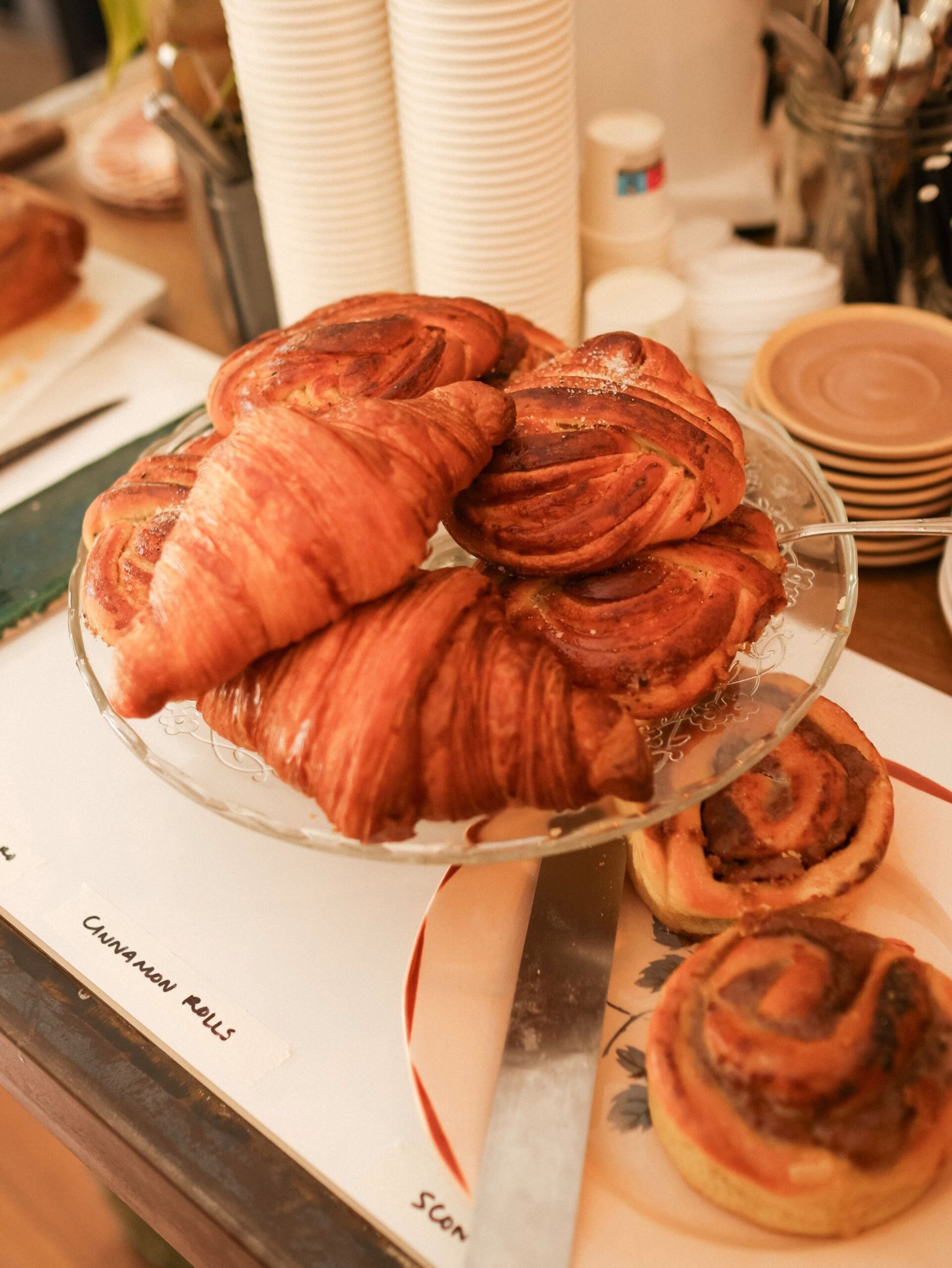 A glass plate filled with croissants and cinnamon rolls on a table.