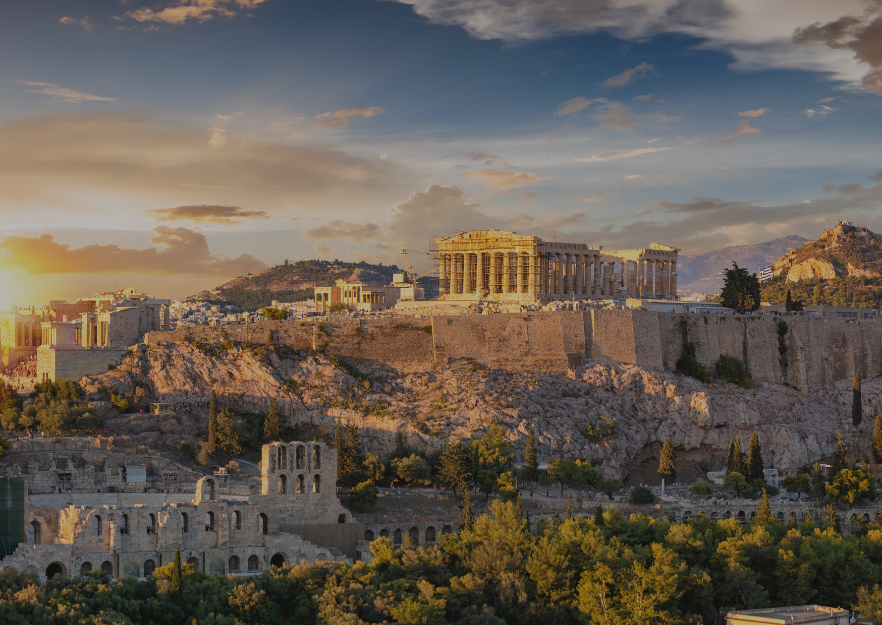 The ancient city of athens is surrounded by trees and mountains at sunset.