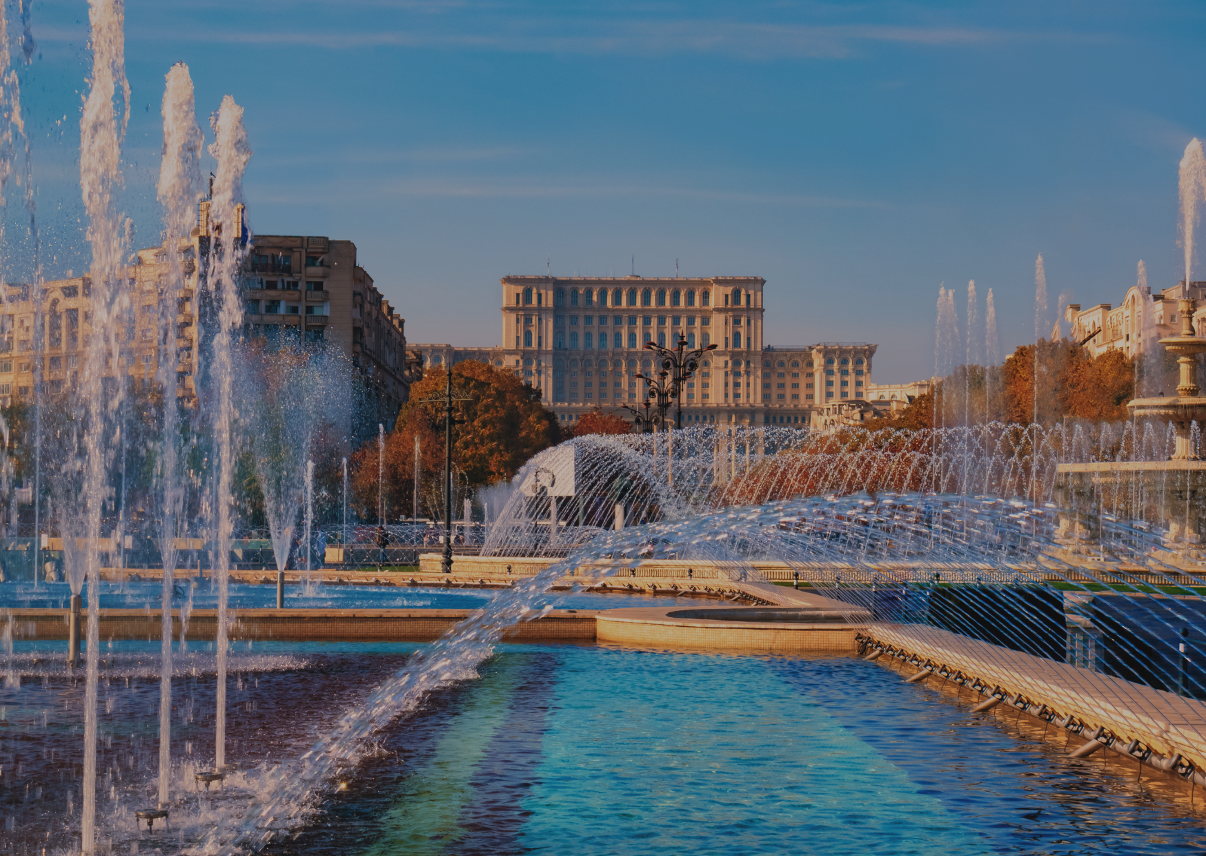 A fountain in a park with a large building in the background.