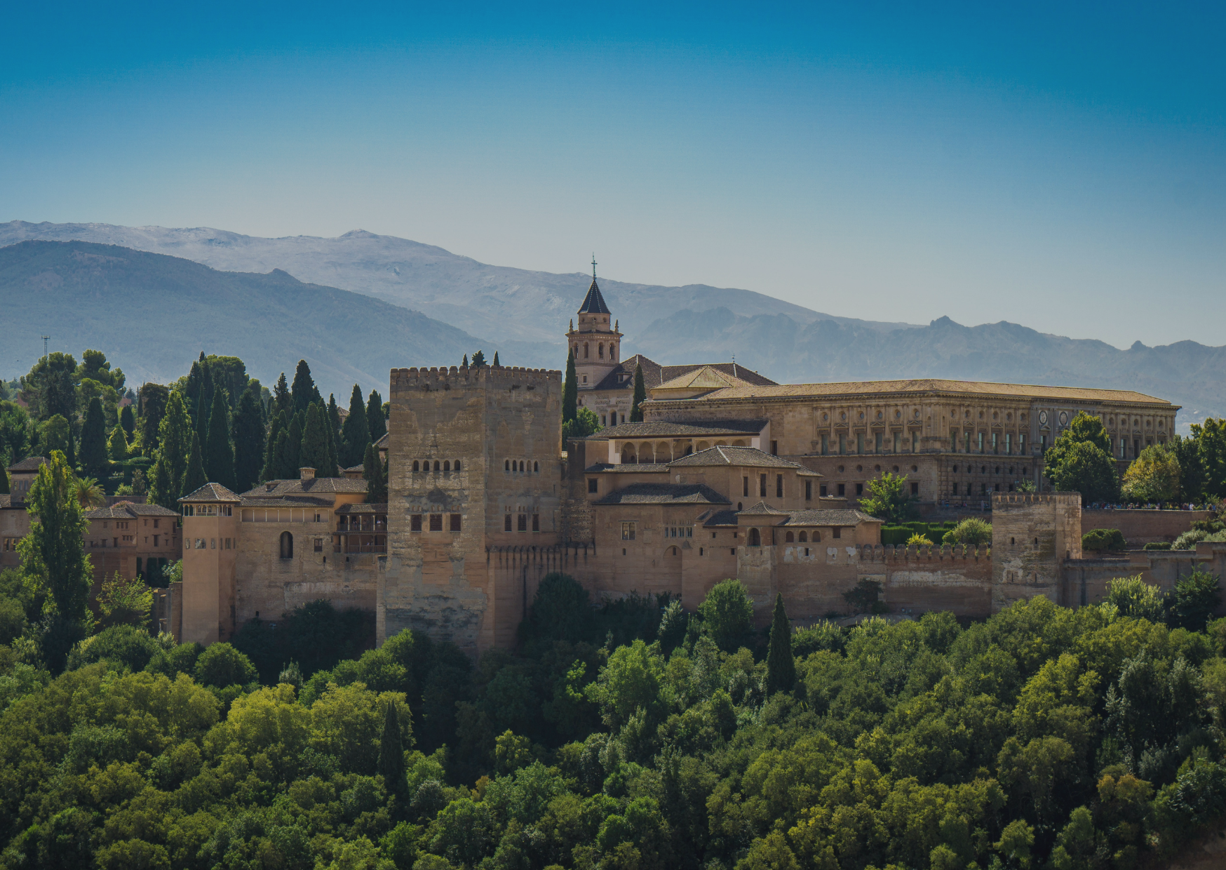An aerial view of a castle surrounded by trees and mountains.
