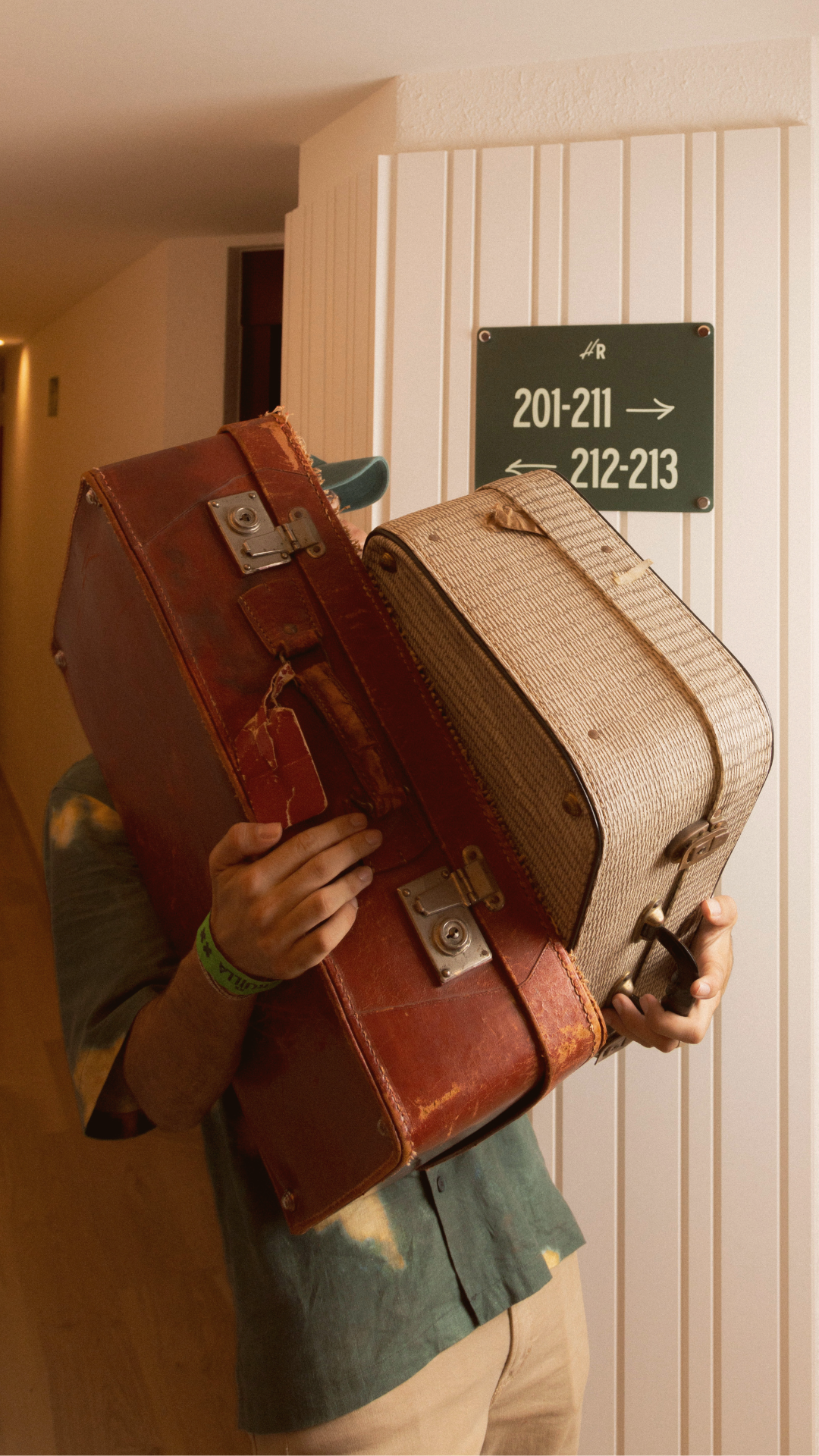 A man is carrying two suitcases in a hallway.