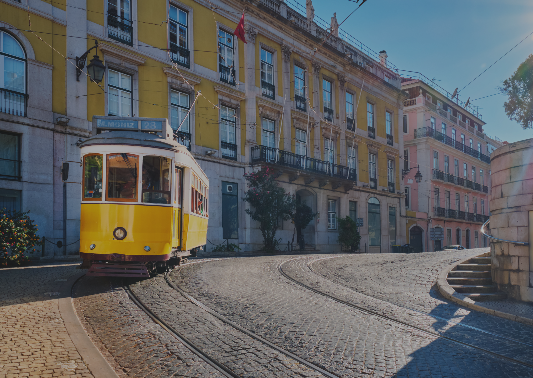 A yellow trolley is driving down a cobblestone street in front of a building.