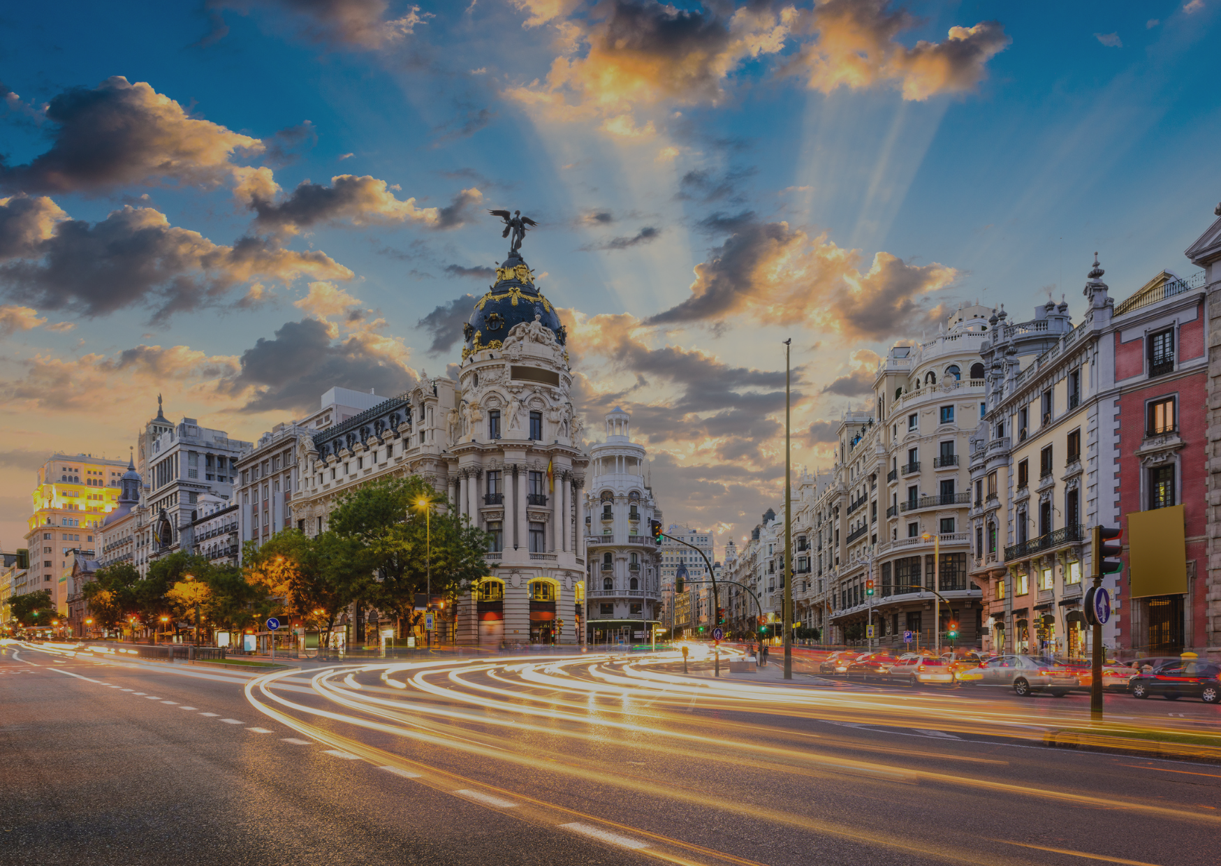 A city street with a large building in the background at sunset.