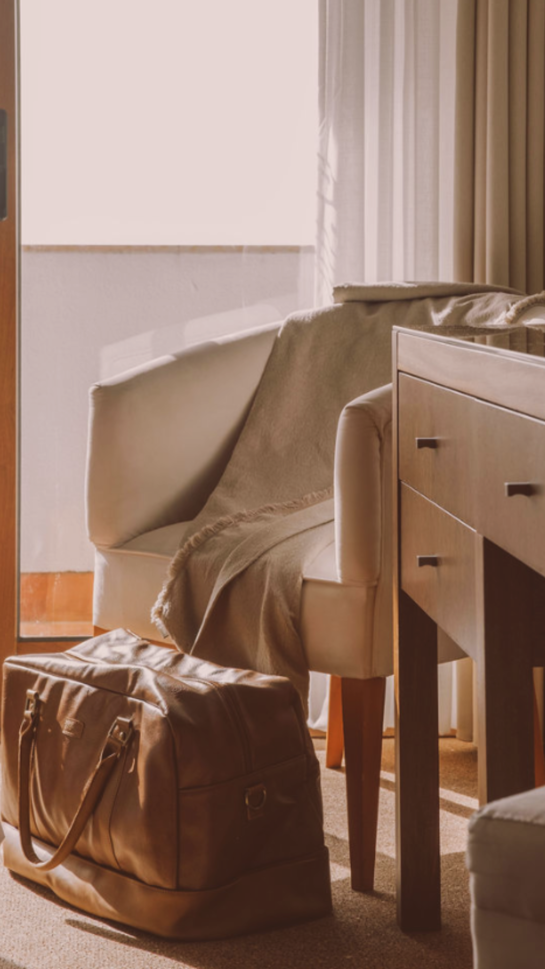 A bag is sitting on the floor next to a chair in a hotel room.