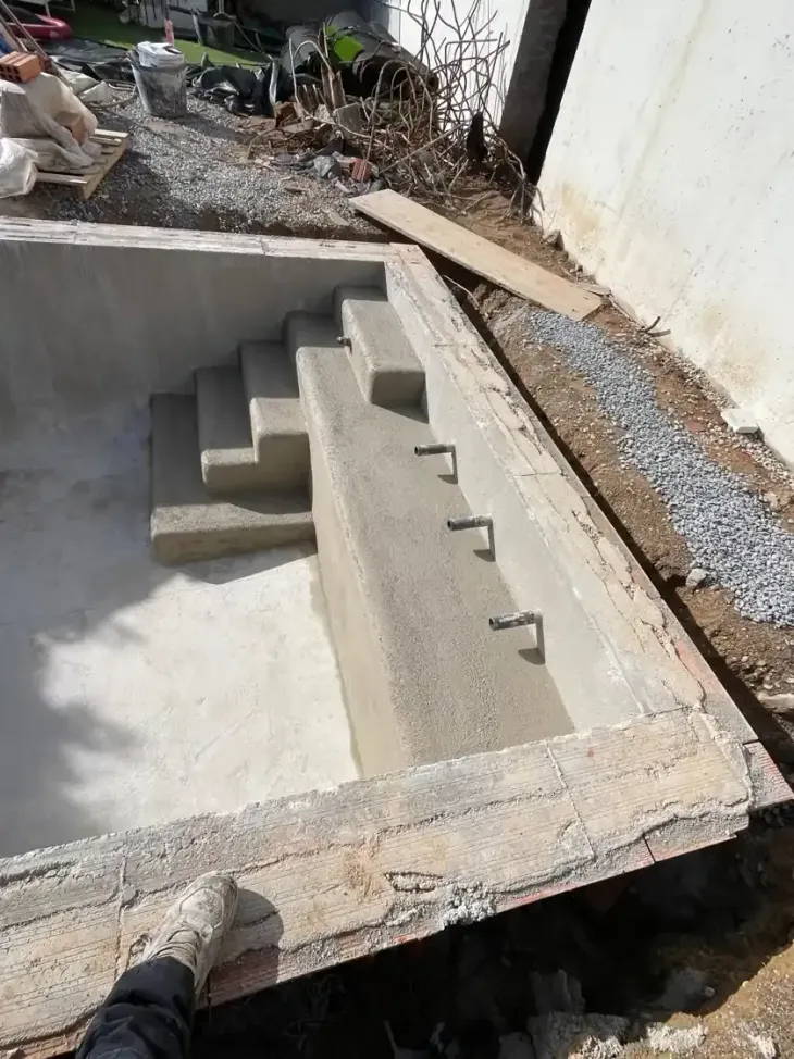 Escalera exterior de hormigón en construcción junto a una pared blanca y un camino de grava.