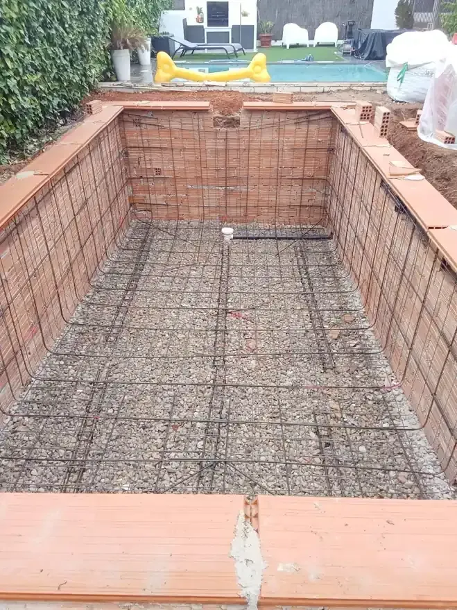 Piscina vacía revestida de ladrillos, en construcción, con suelo de barras de acero.