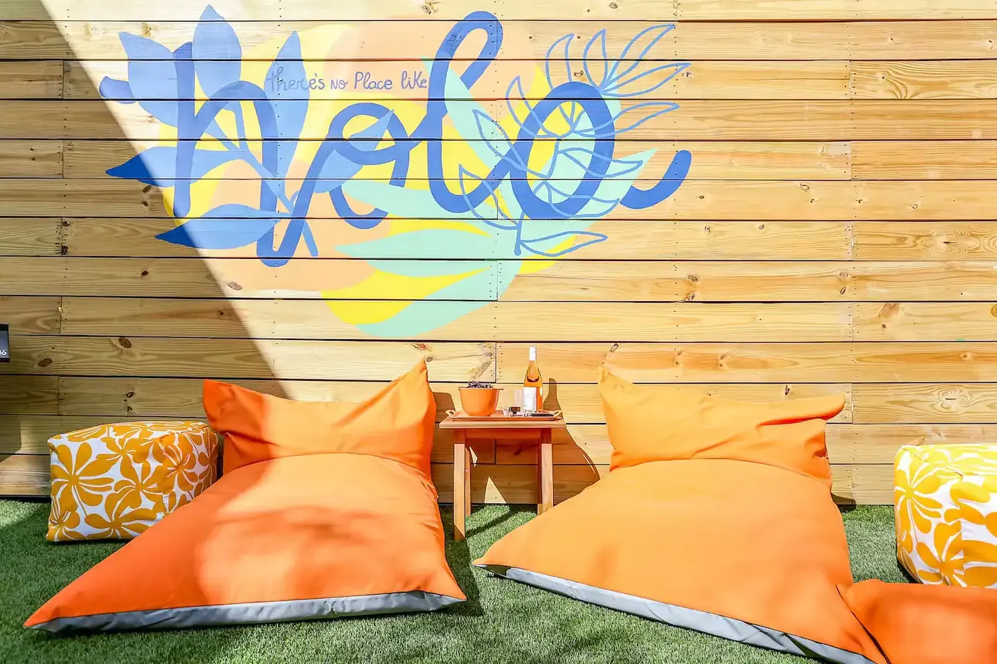 Two orange bean bag chairs are sitting on the grass in front of a wooden wall.