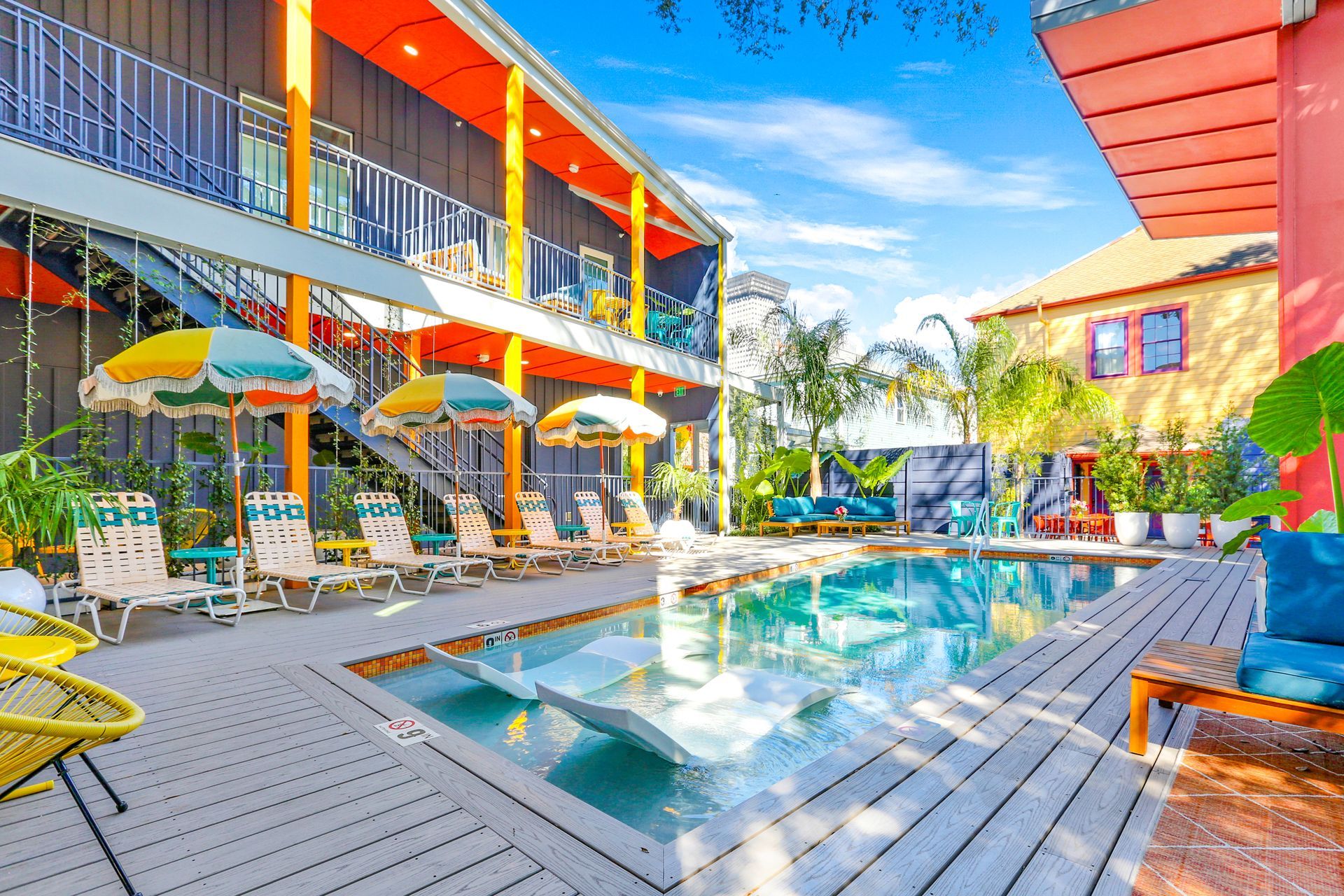 A large swimming pool surrounded by chairs and umbrellas in front of a hotel.