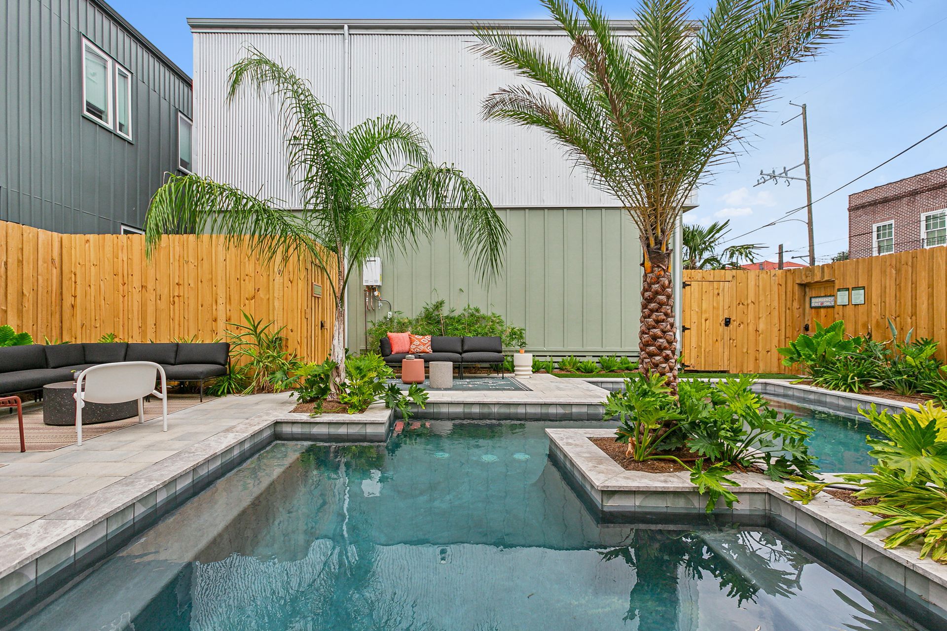 A large swimming pool is surrounded by a wooden fence and a palm tree.