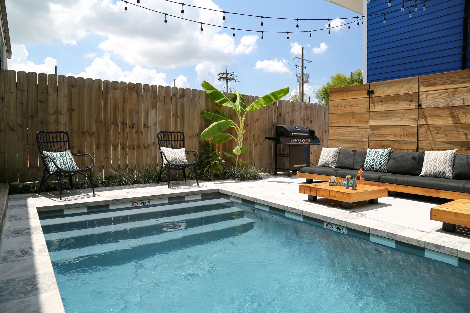 A large swimming pool is surrounded by a wooden fence and patio furniture.