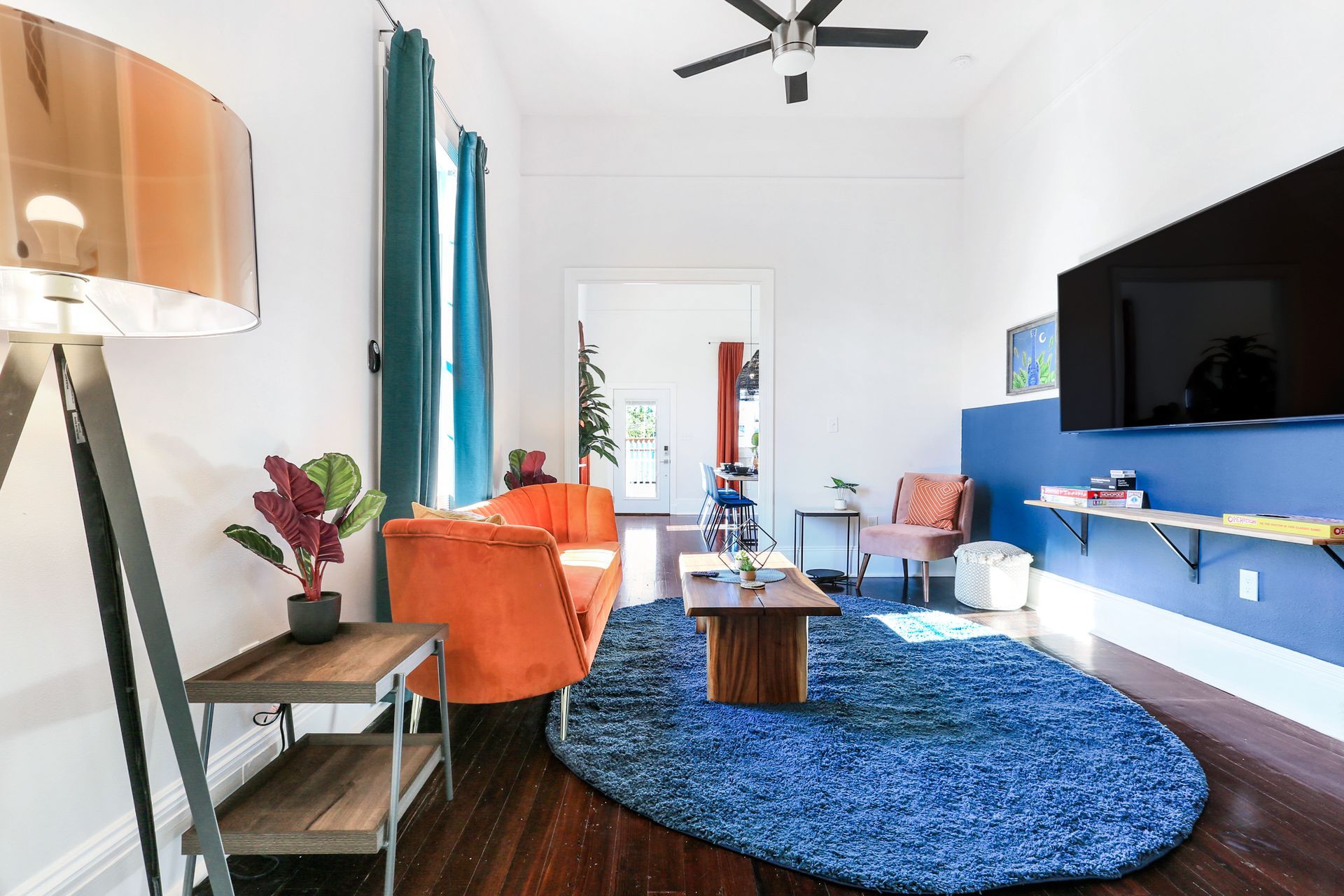 A living room with a blue rug , orange chairs , a coffee table and a flat screen tv.