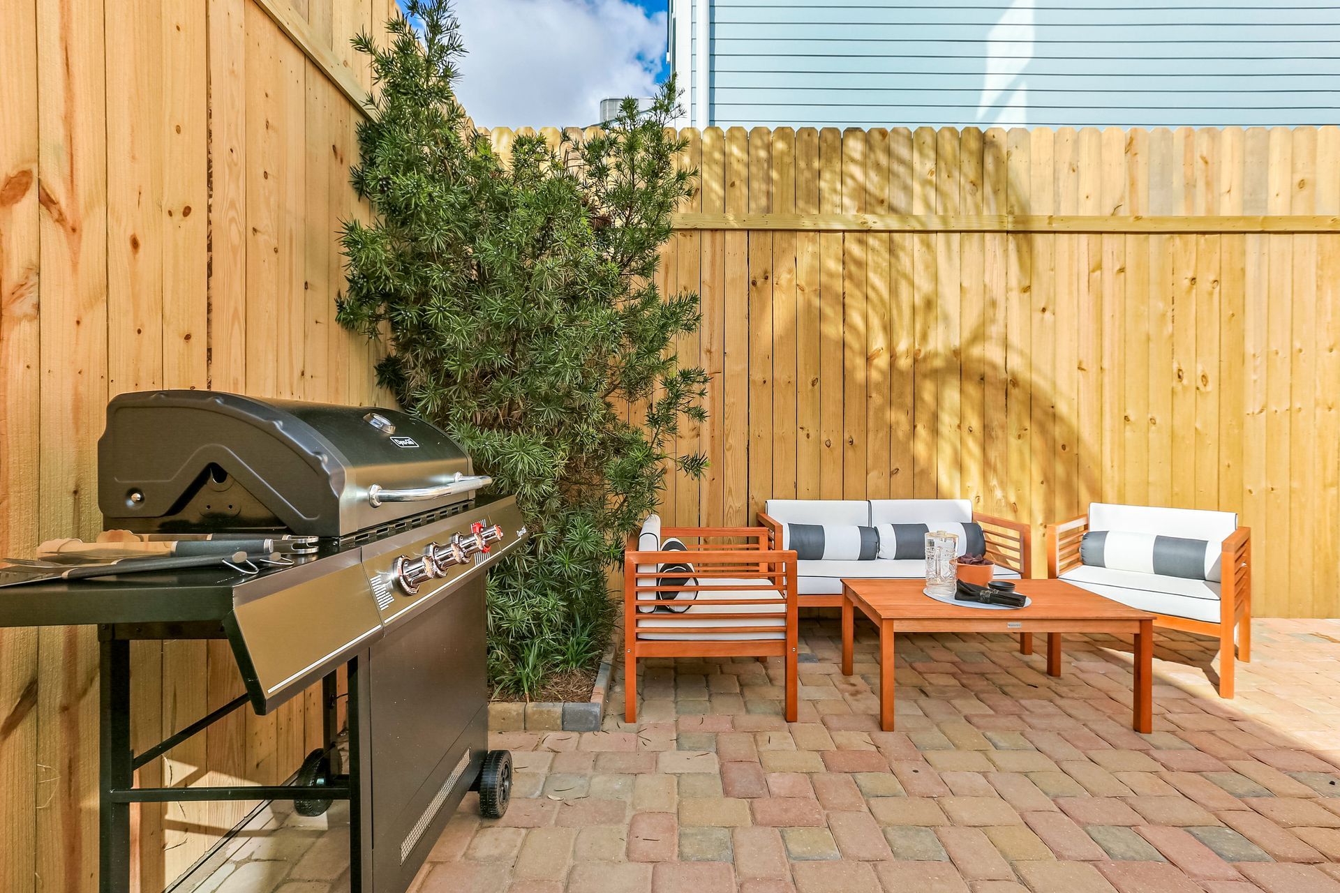A patio with a grill , couch , table and chairs behind a wooden fence.