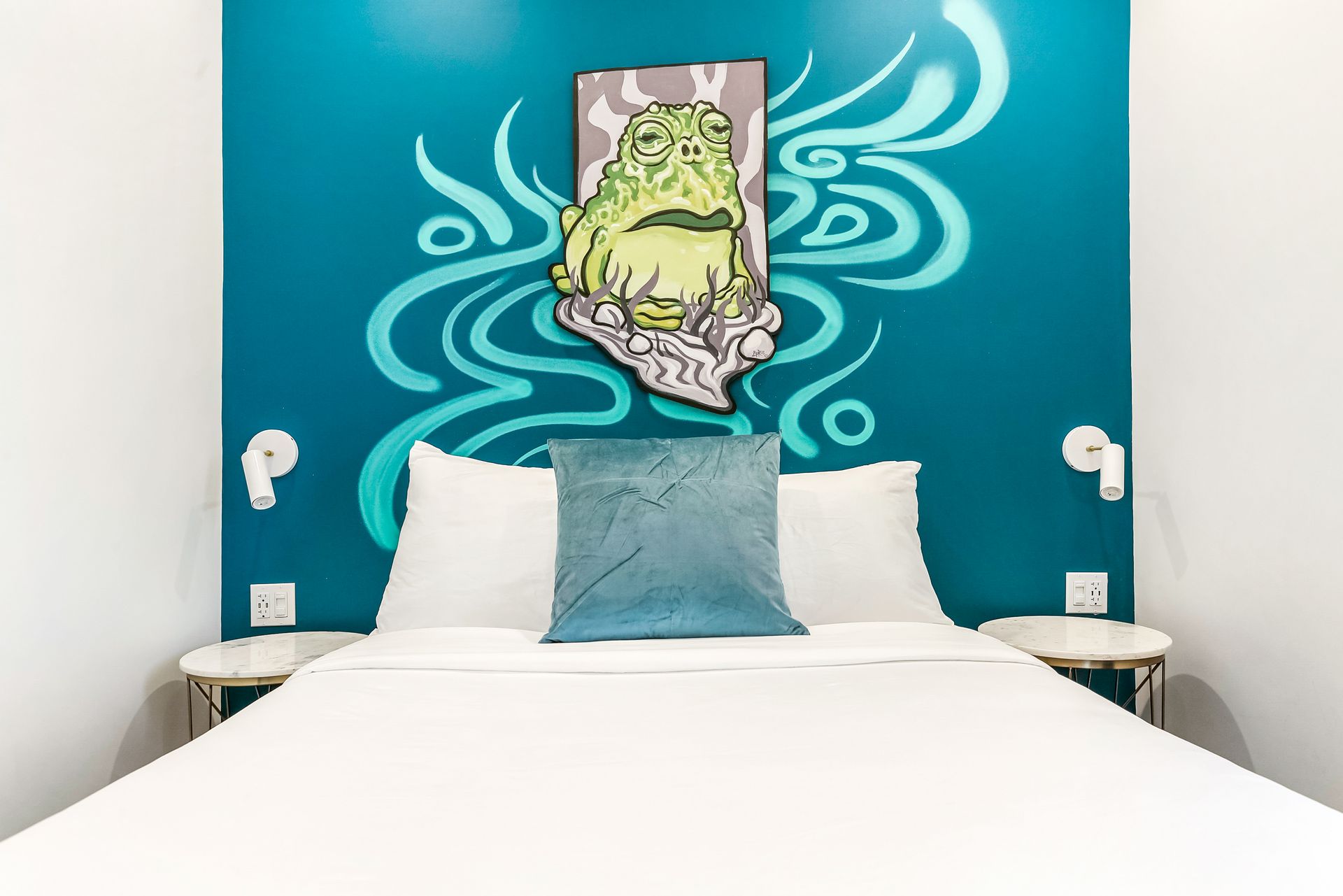 A bed with a picture of a frog on the wall behind it.