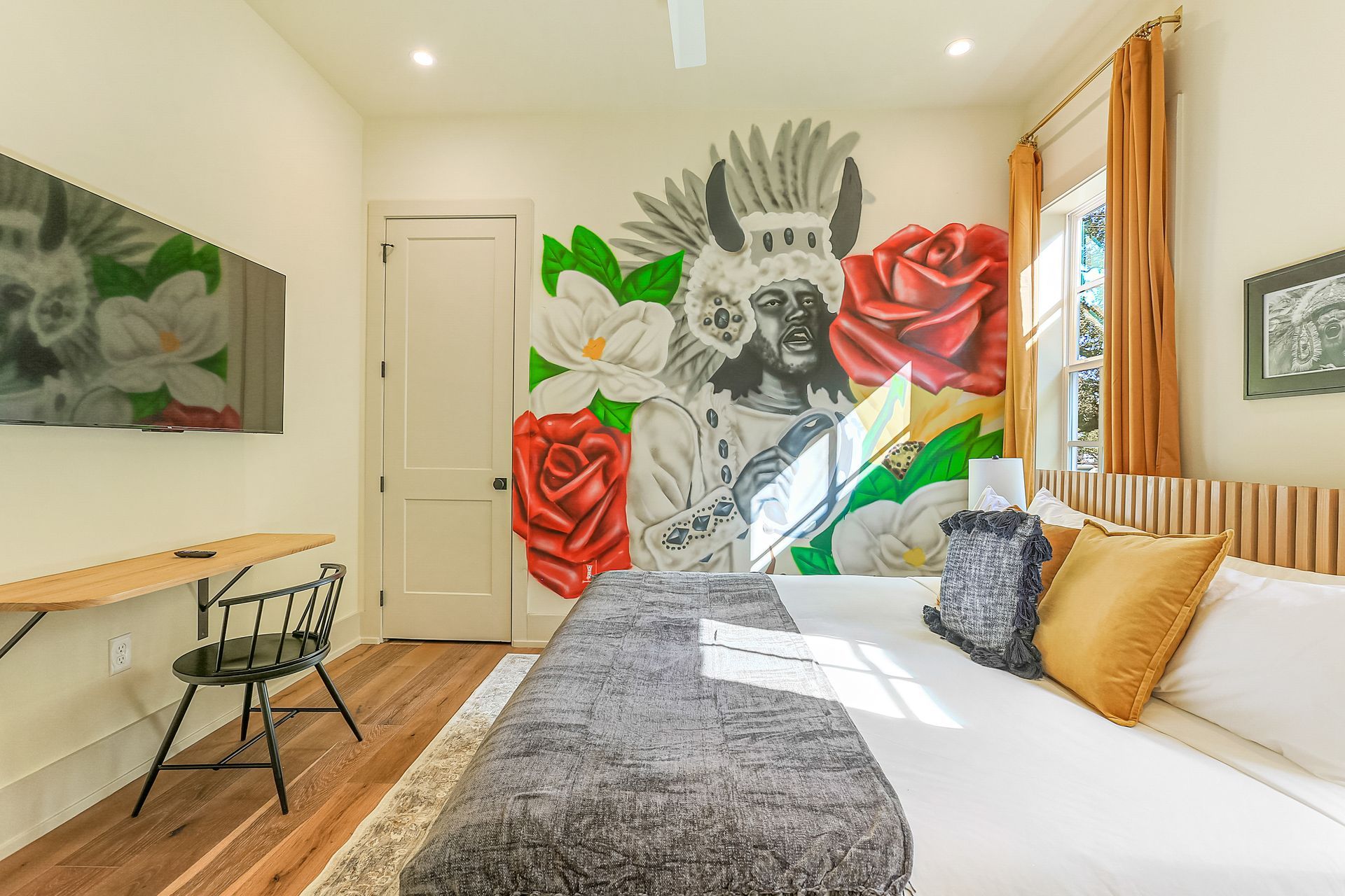 A bedroom with a bed , desk , television and a mural on the wall.