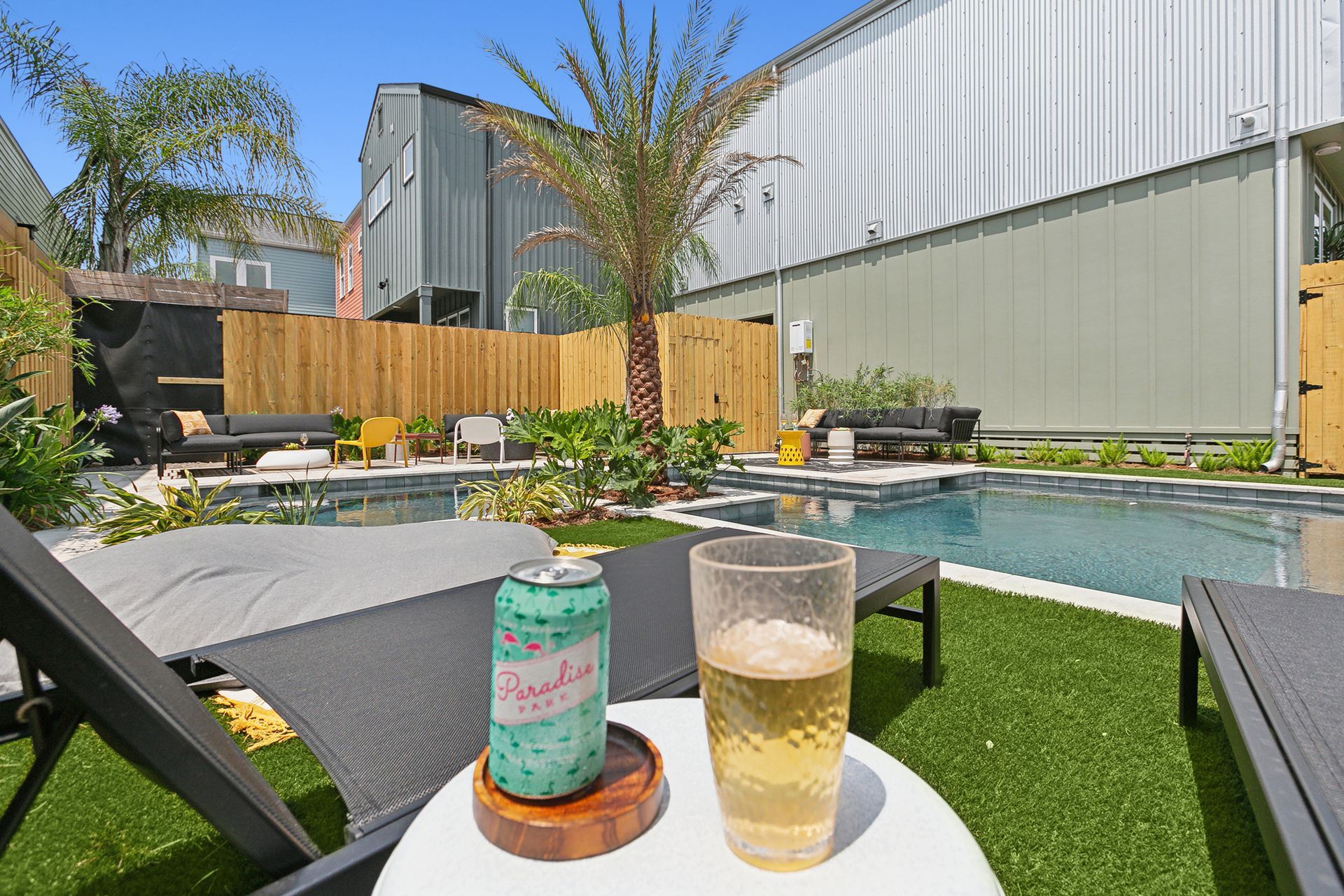 A can of soda and a glass of beer are on a table in front of a swimming pool.