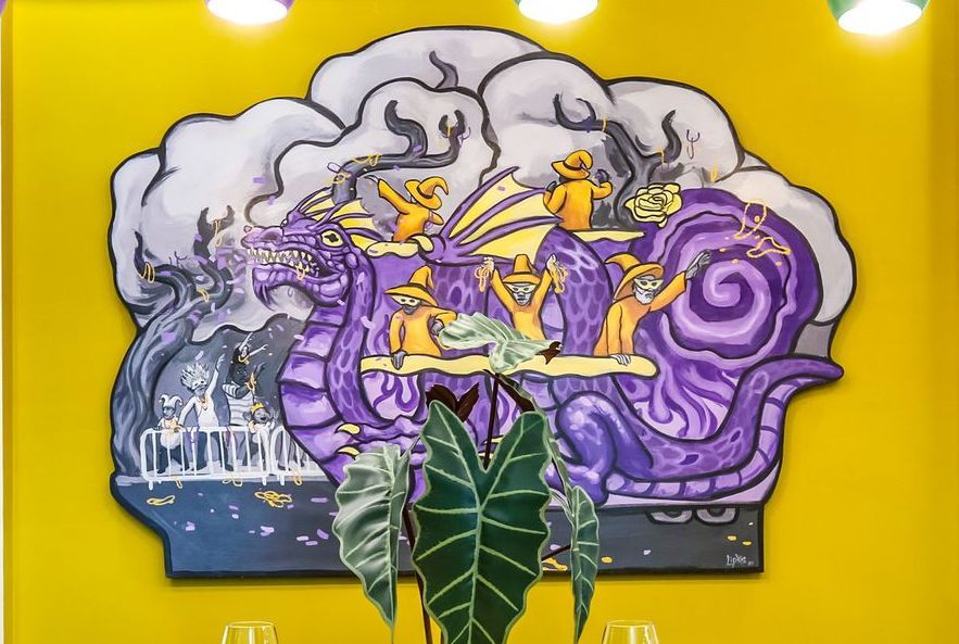 A painting on a yellow wall with a plant in front of it