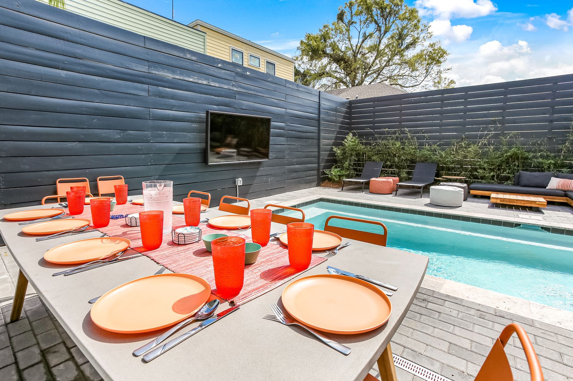 A table with plates and glasses on it in front of a swimming pool.