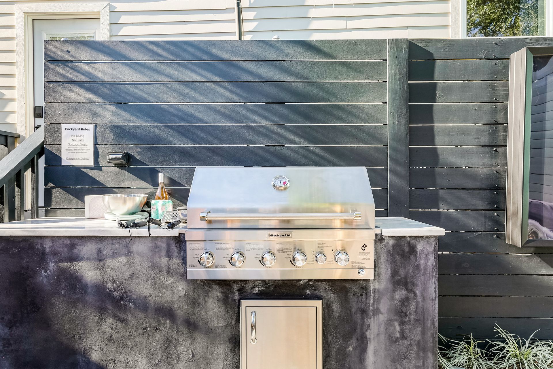 A stainless steel grill is sitting in front of a wooden fence.