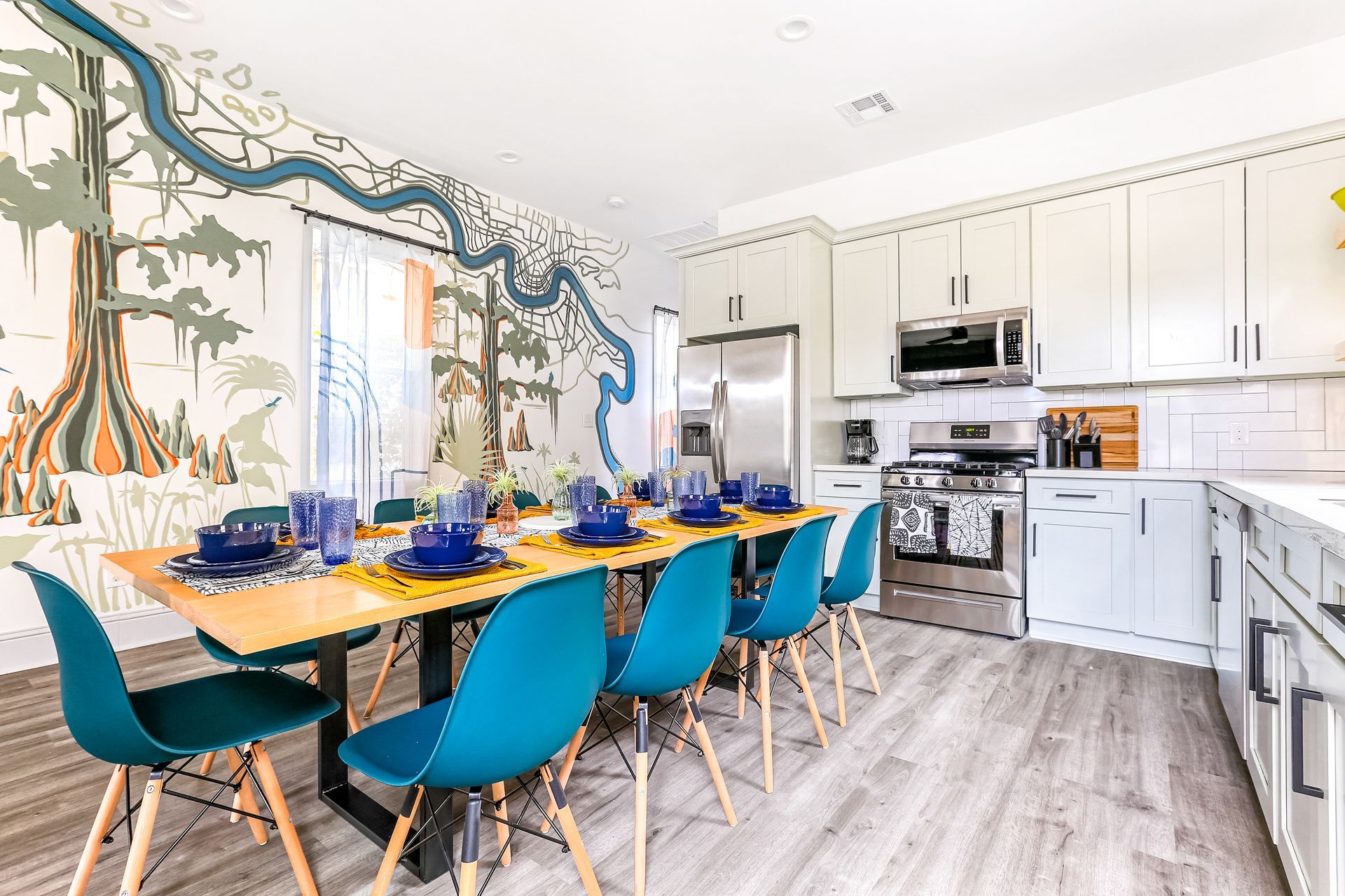A kitchen with a long table and chairs and a mural on the wall.