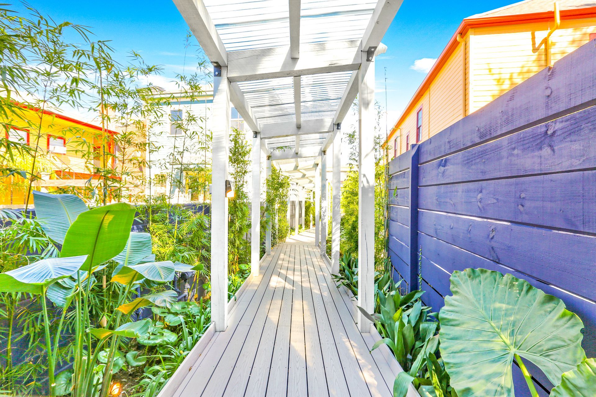 A wooden walkway surrounded by plants and a blue fence.