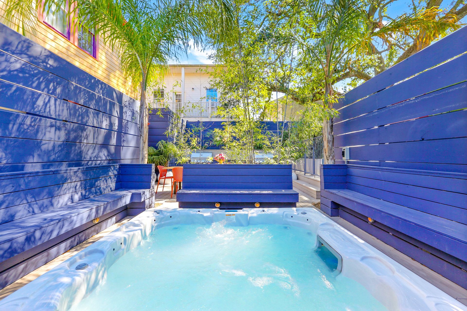 A hot tub surrounded by blue benches and a blue fence in a backyard.