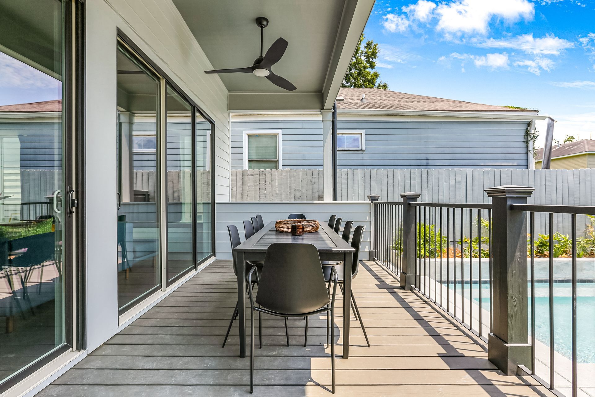 A patio with a table and chairs and a ceiling fan next to a pool.