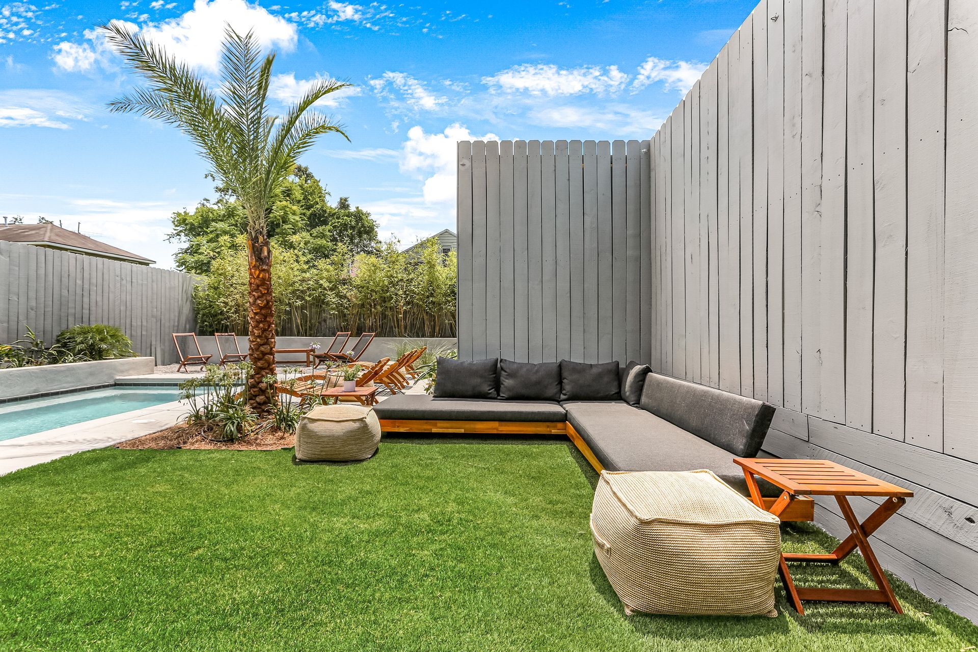 There is a swimming pool in the backyard with a couch and ottomans.