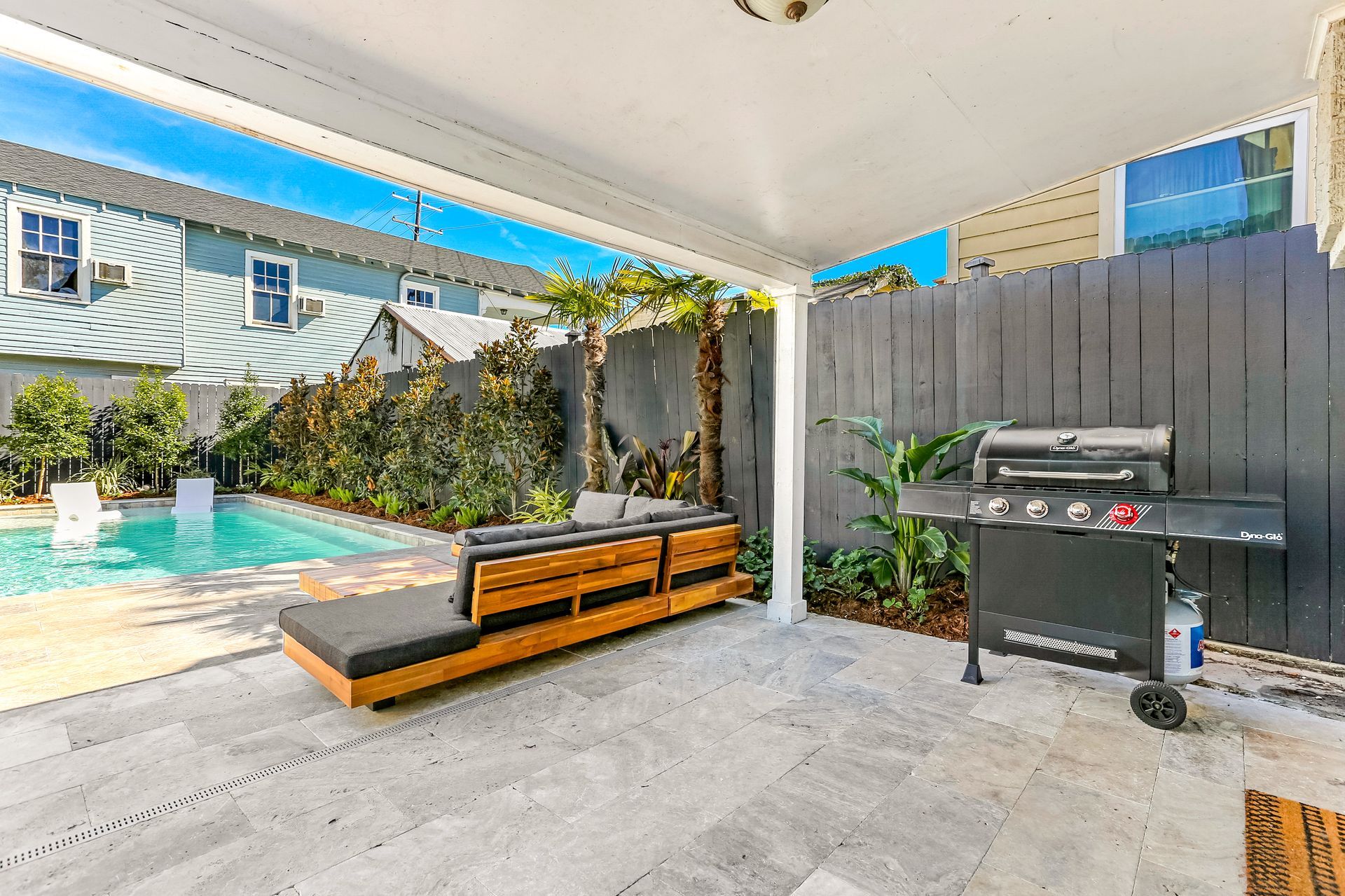 A patio with a grill and a swimming pool in the background.