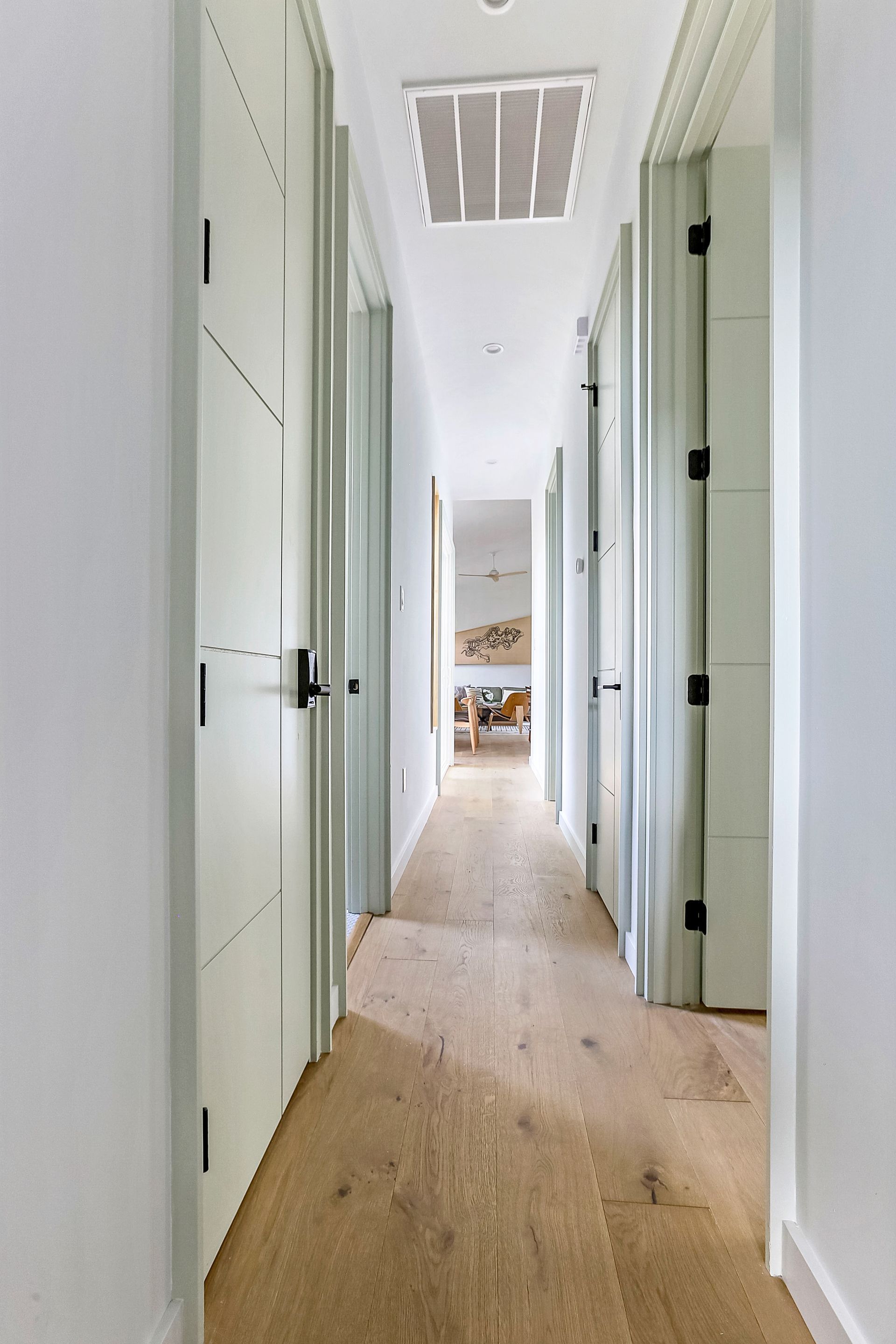 A long hallway with wooden floors and white doors leading to a bedroom.