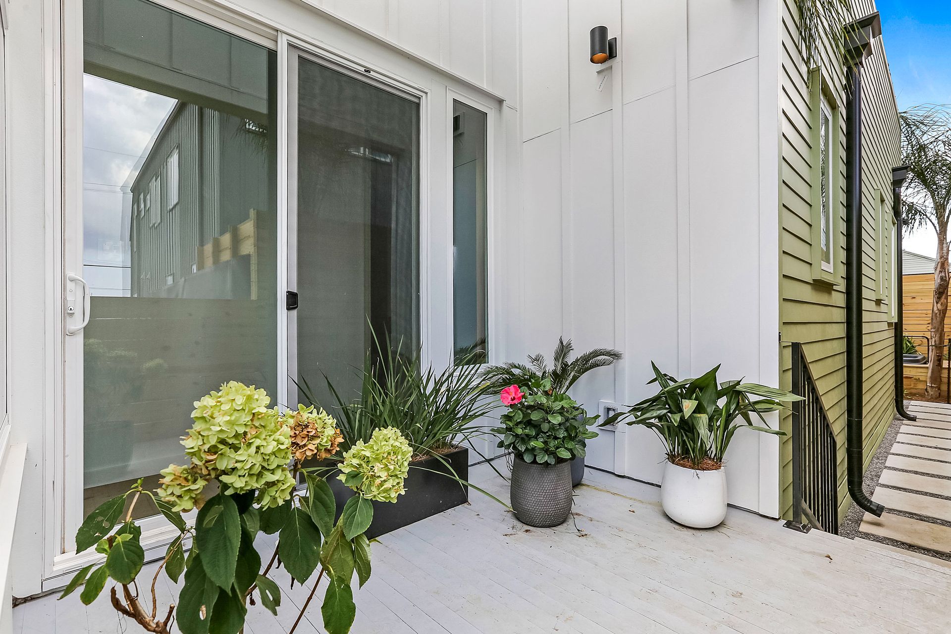 A patio with potted plants and flowers in front of a sliding glass door.