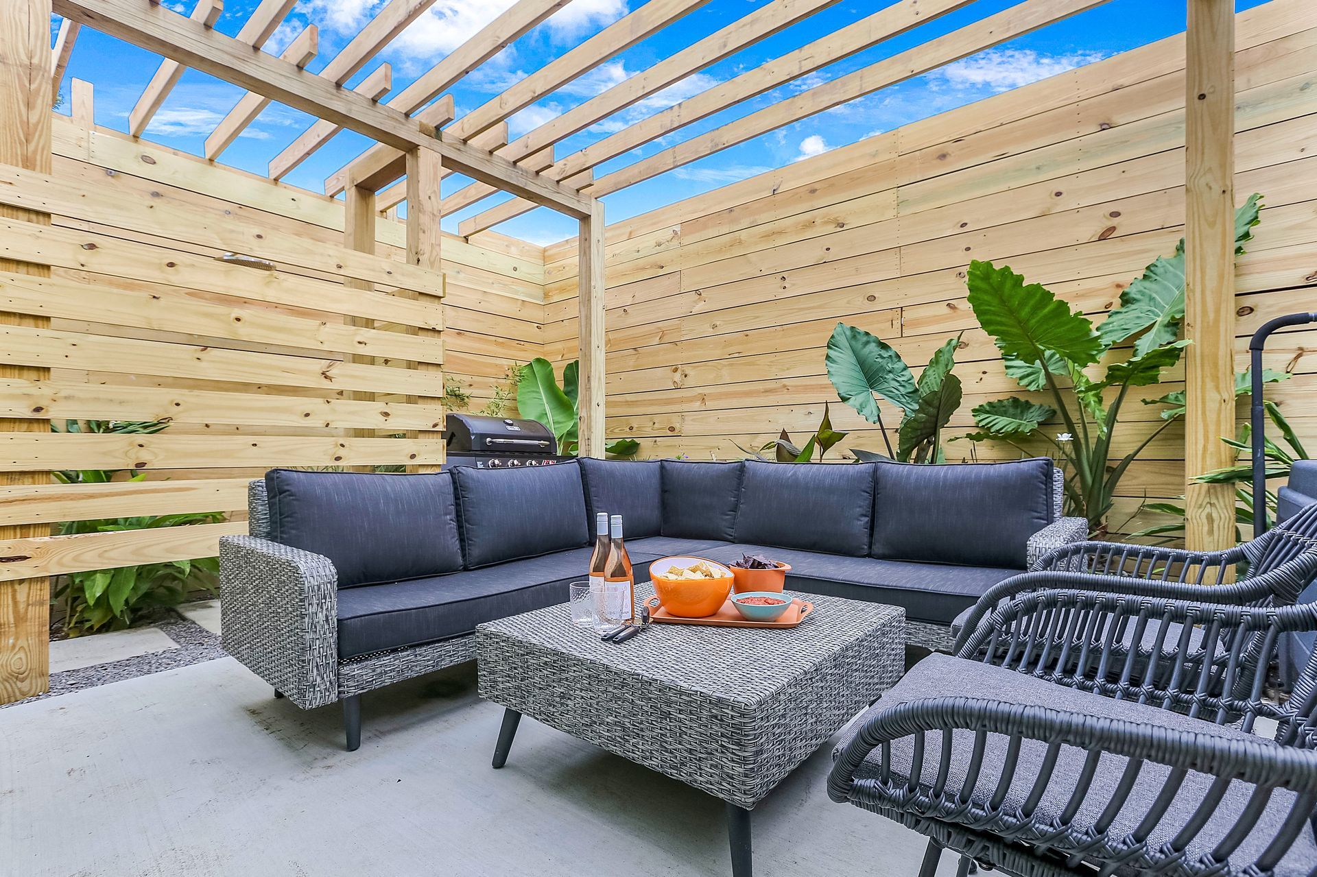 A patio with a couch , chairs , and a table under a pergola.