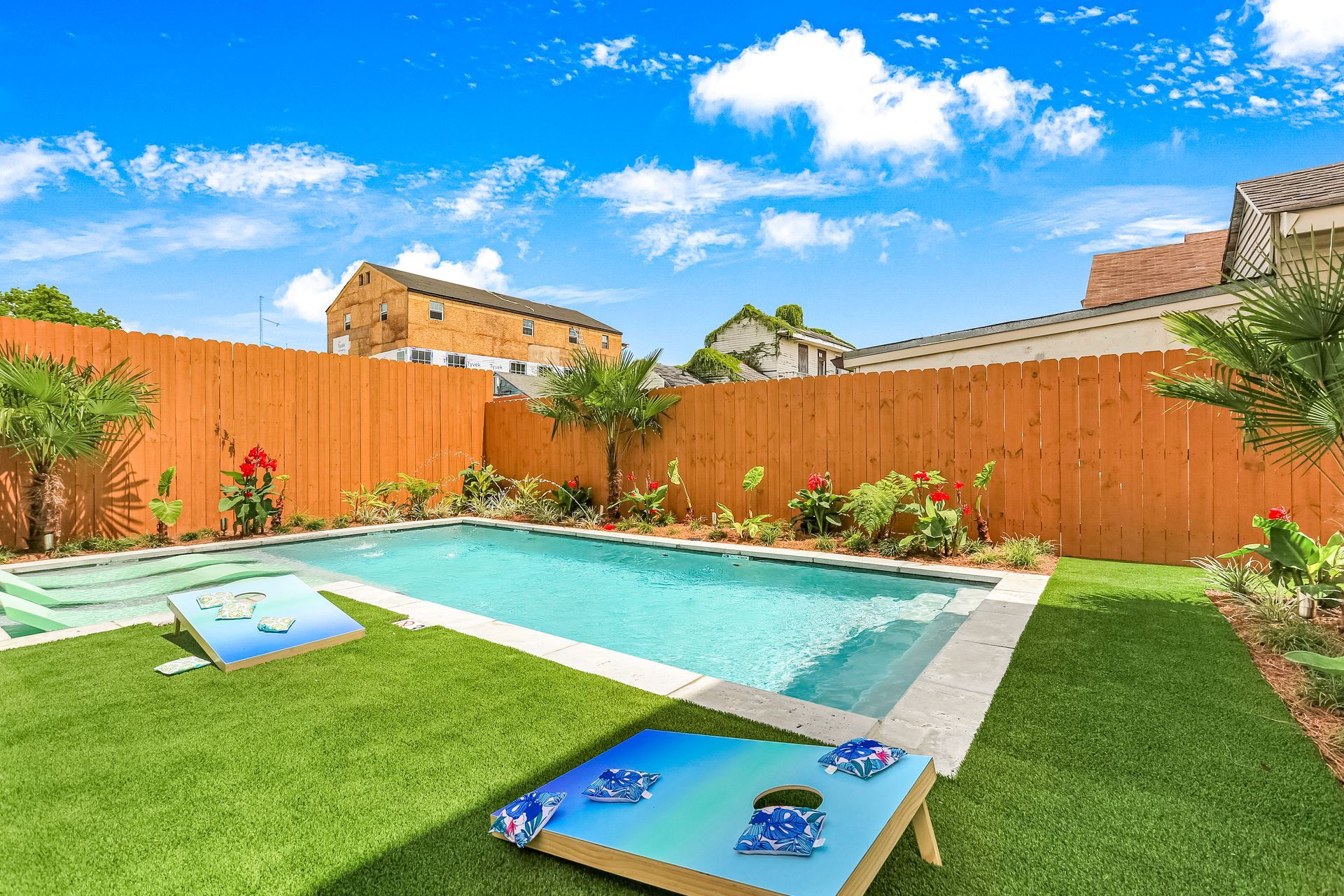 A backyard with a pool and a cornhole board.
