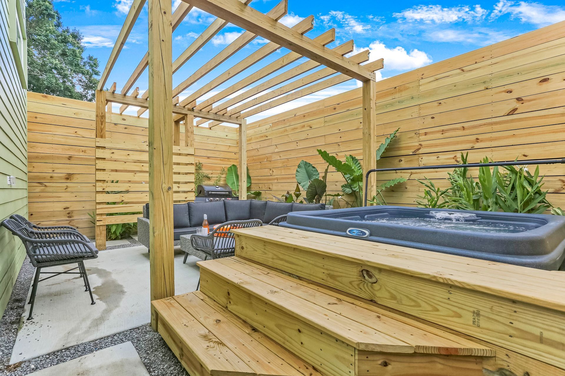 A hot tub is sitting under a wooden pergola in a backyard.