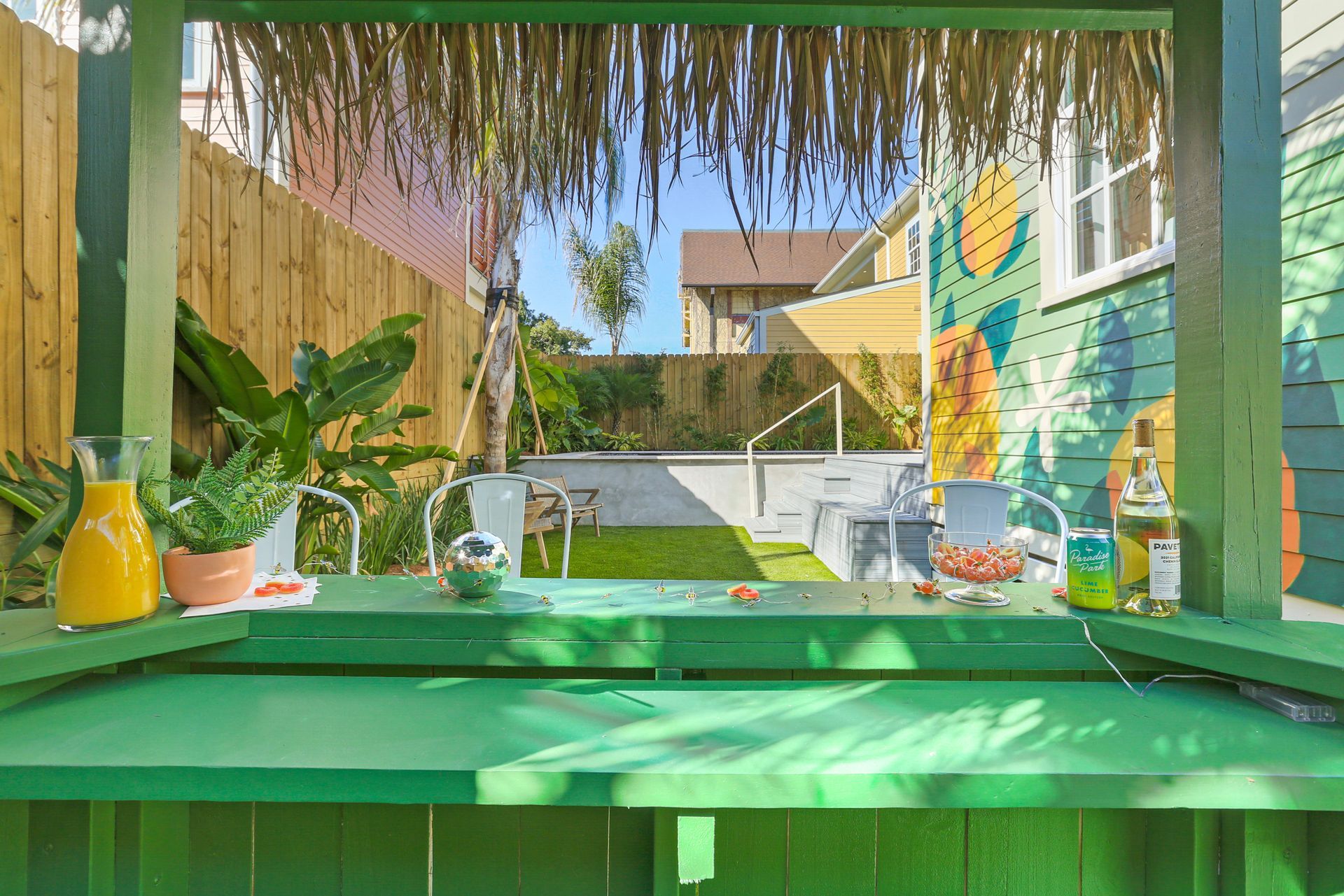 A green bar with a thatched roof is sitting in the backyard of a house.