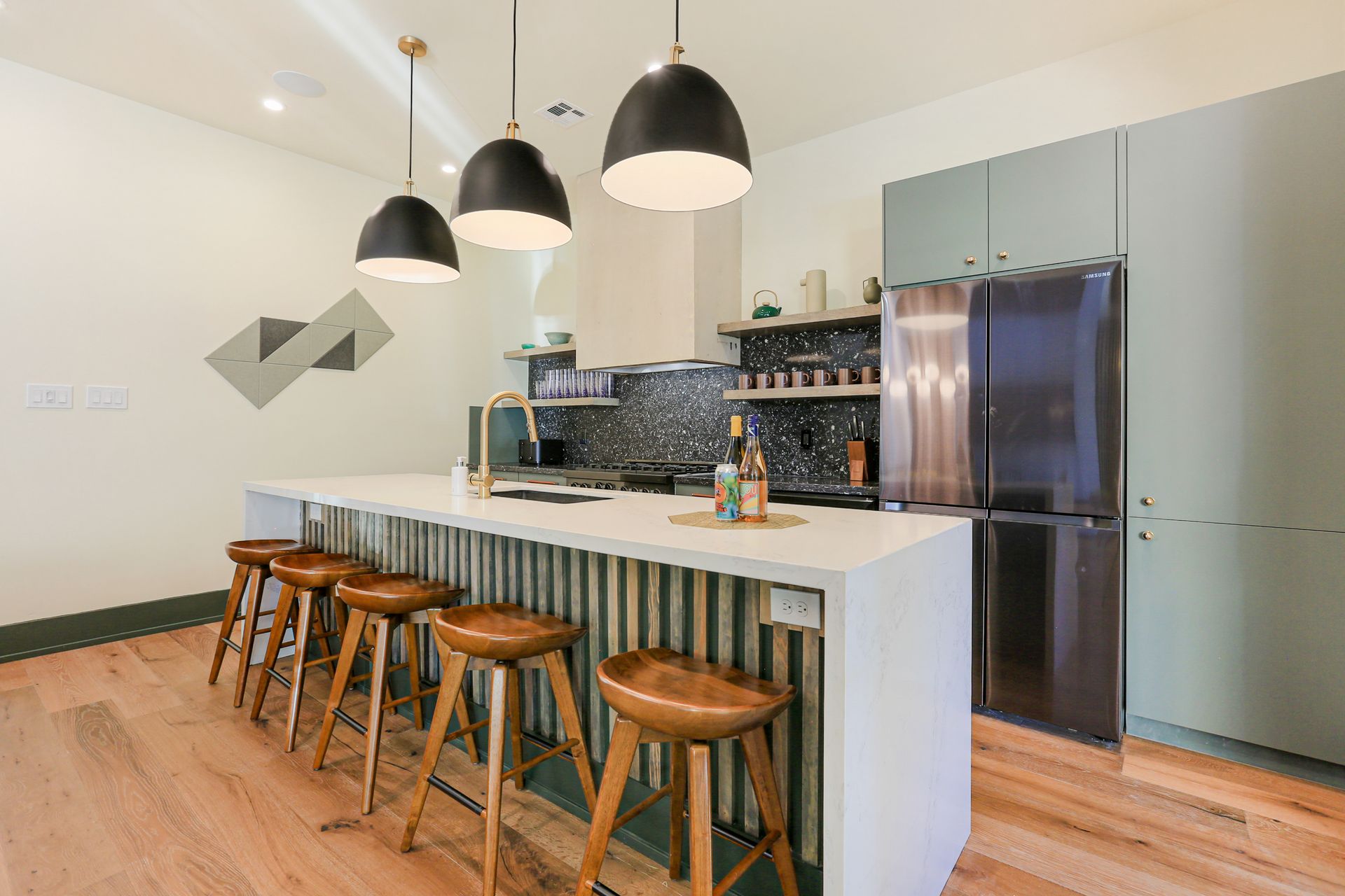 A kitchen with a long island , stools and a refrigerator.