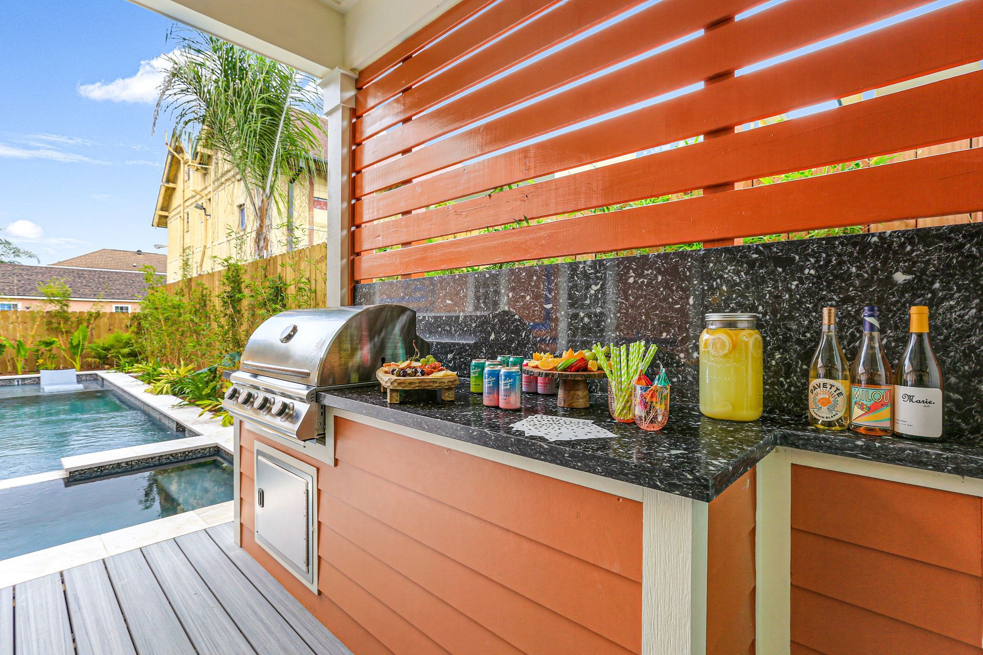 A kitchen with a grill and bottles on the counter next to a pool.