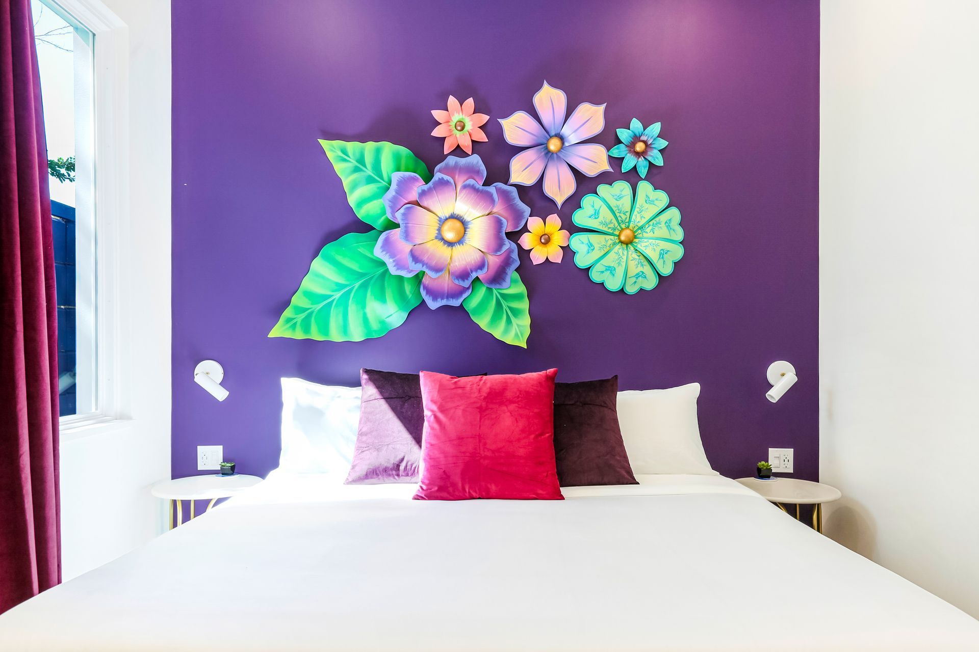 A bedroom with a bed and a purple wall with flowers painted on it.