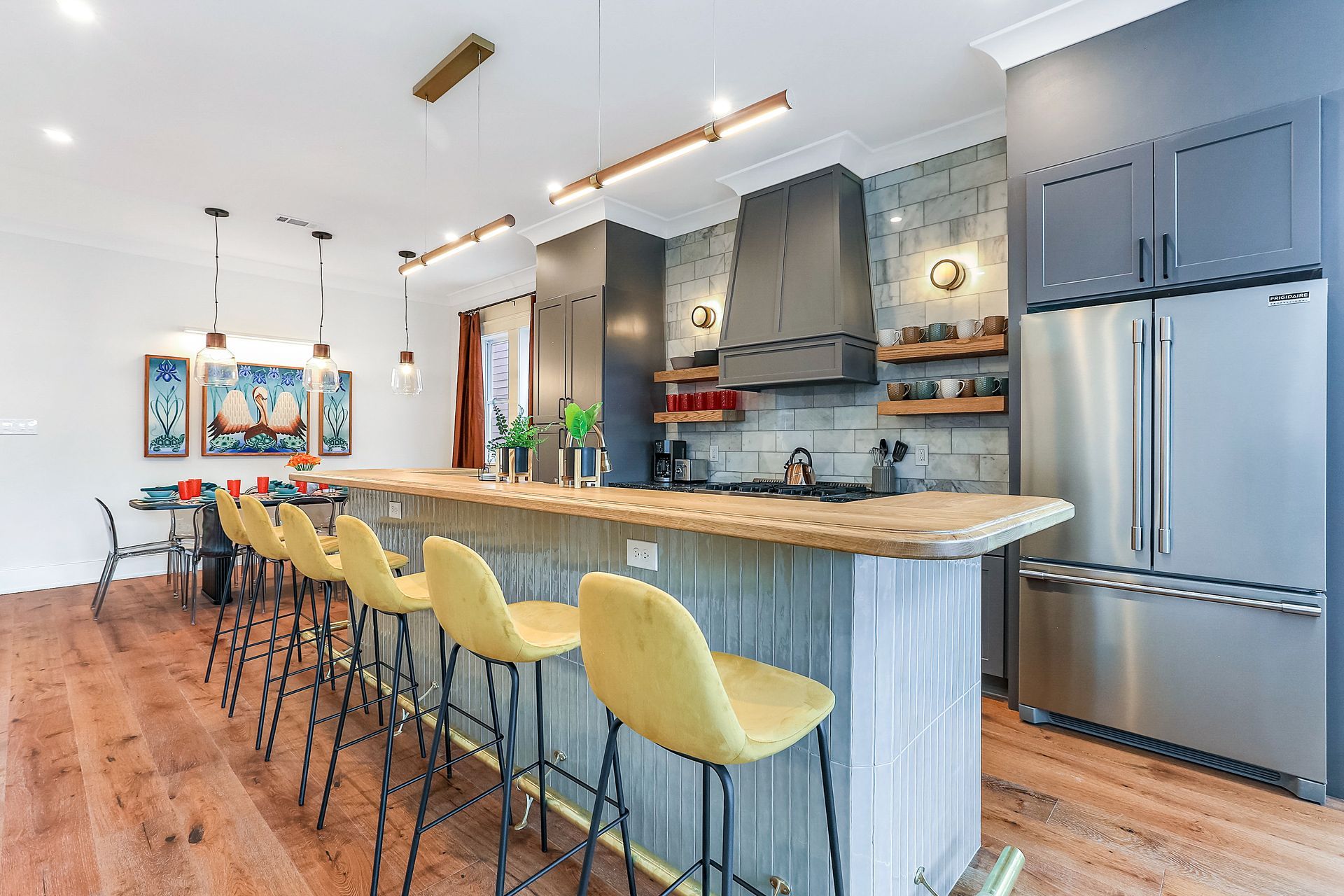 A kitchen with stainless steel appliances , a large island , and yellow bar stools.