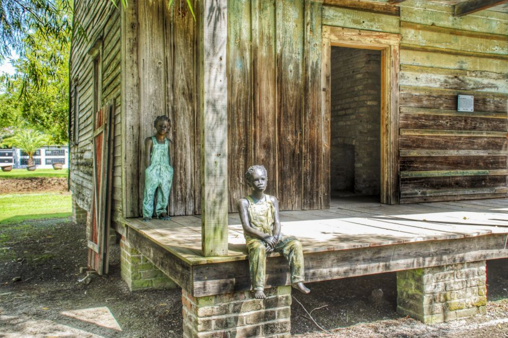 A statue of two children sitting on the porch of a log cabin.