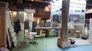 Un stand de feria comercial con elementos arquitectónicos de piedra, una mesa con sillas y una gran columna central.