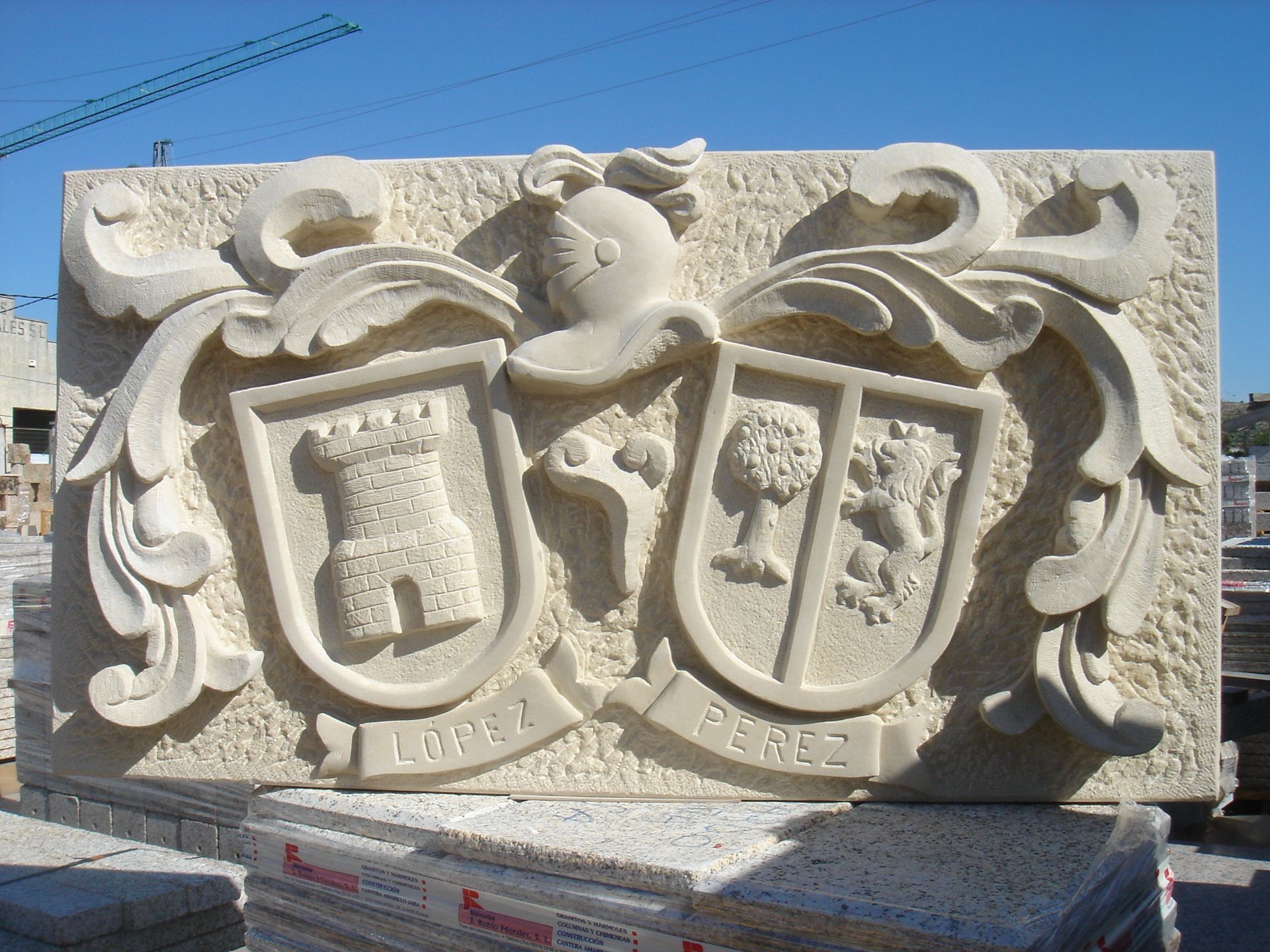 Una talla de piedra de color claro que representa dos escudos heráldicos con nombres de familia, con un castillo, un árbol y un emblema de león.