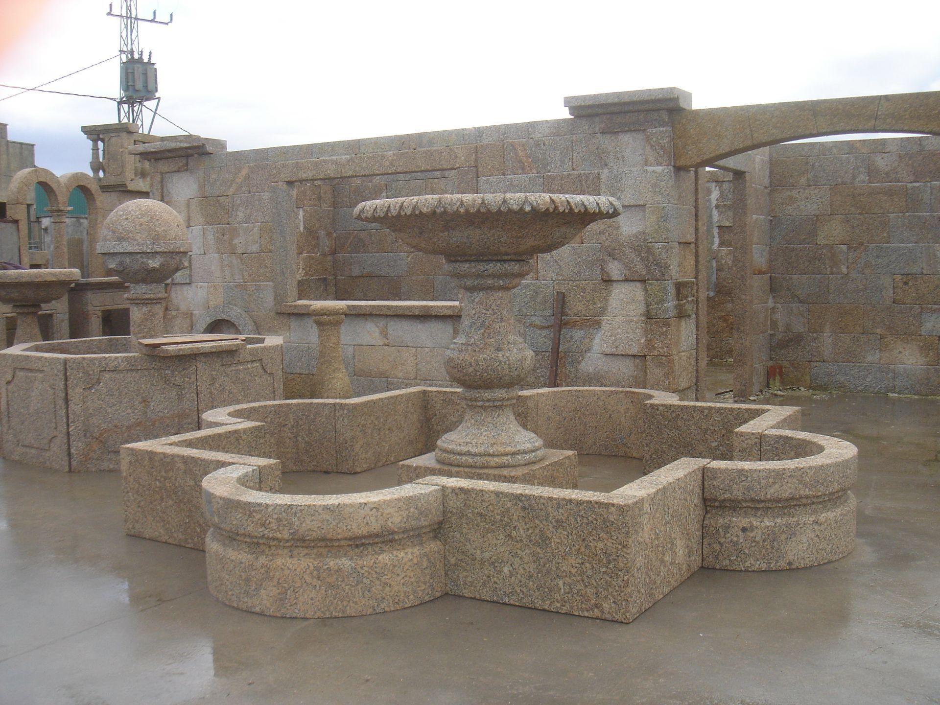 Una fuente de piedra con una pila en forma de cuadrifolio se alza al aire libre en un patio de mampostería.