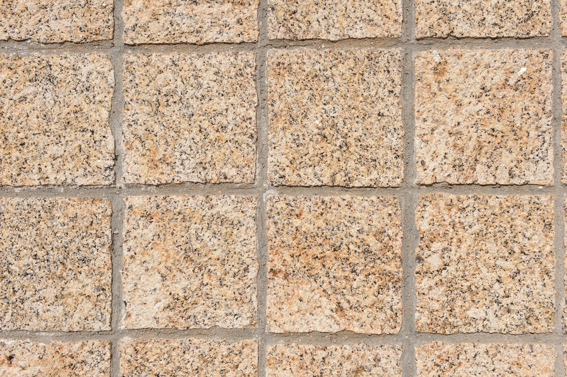 Primer plano de una cuadrícula de adoquines cuadrados de granito de color tostado, separados por finas líneas de lechada de color gris claro.