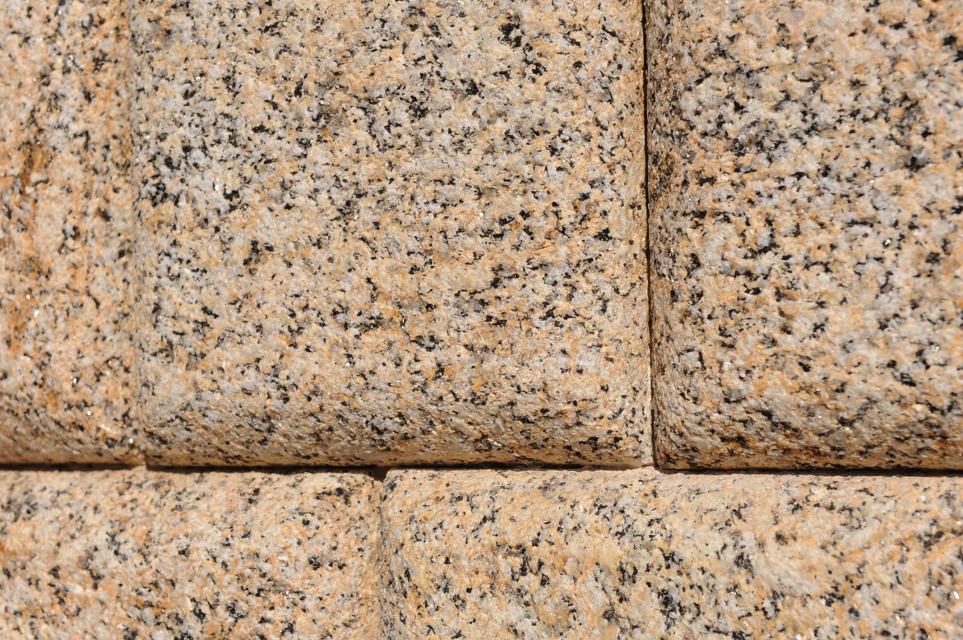 Vista de cerca de bloques de granito beige texturizado con motas negras, dispuestos en un patrón de cuadrícula rectangular.
