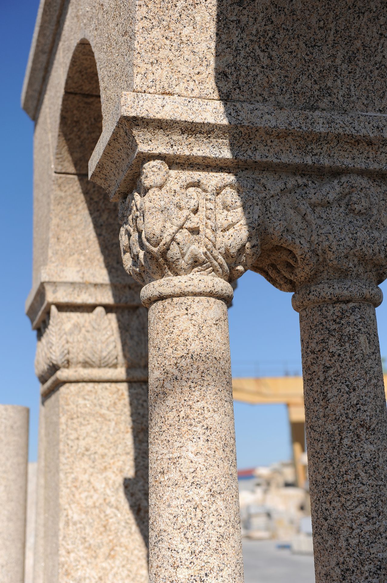 Primer plano de una columna de piedra tallada con capitel y motivos vegetales decorativos, con un cielo azul despejado de fondo.