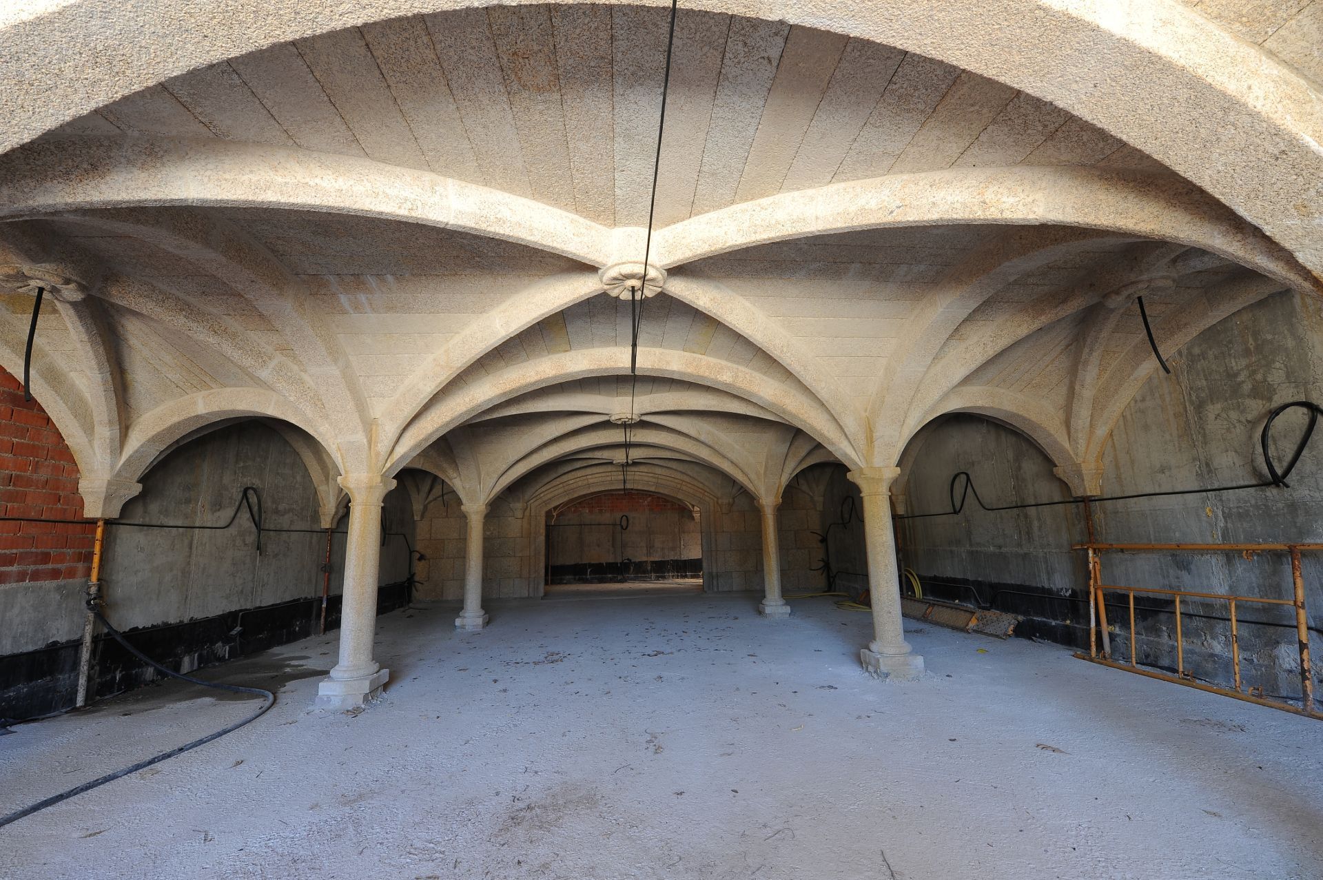 Vista interior de un sótano con techos abovedados, pilares de piedra arqueados y paredes de hormigón sin acabado.