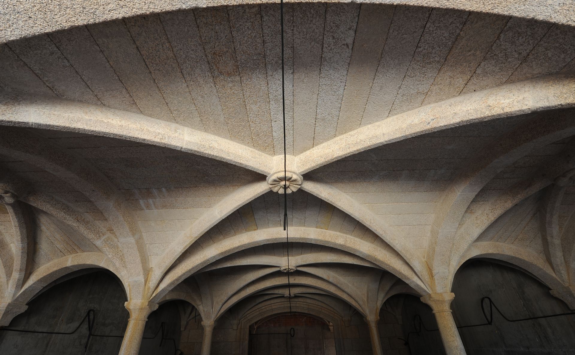 Un techo abovedado de piedra con nervaduras y arcos que se entrecruzan y confluyen en florones ornamentales tallados en el centro.