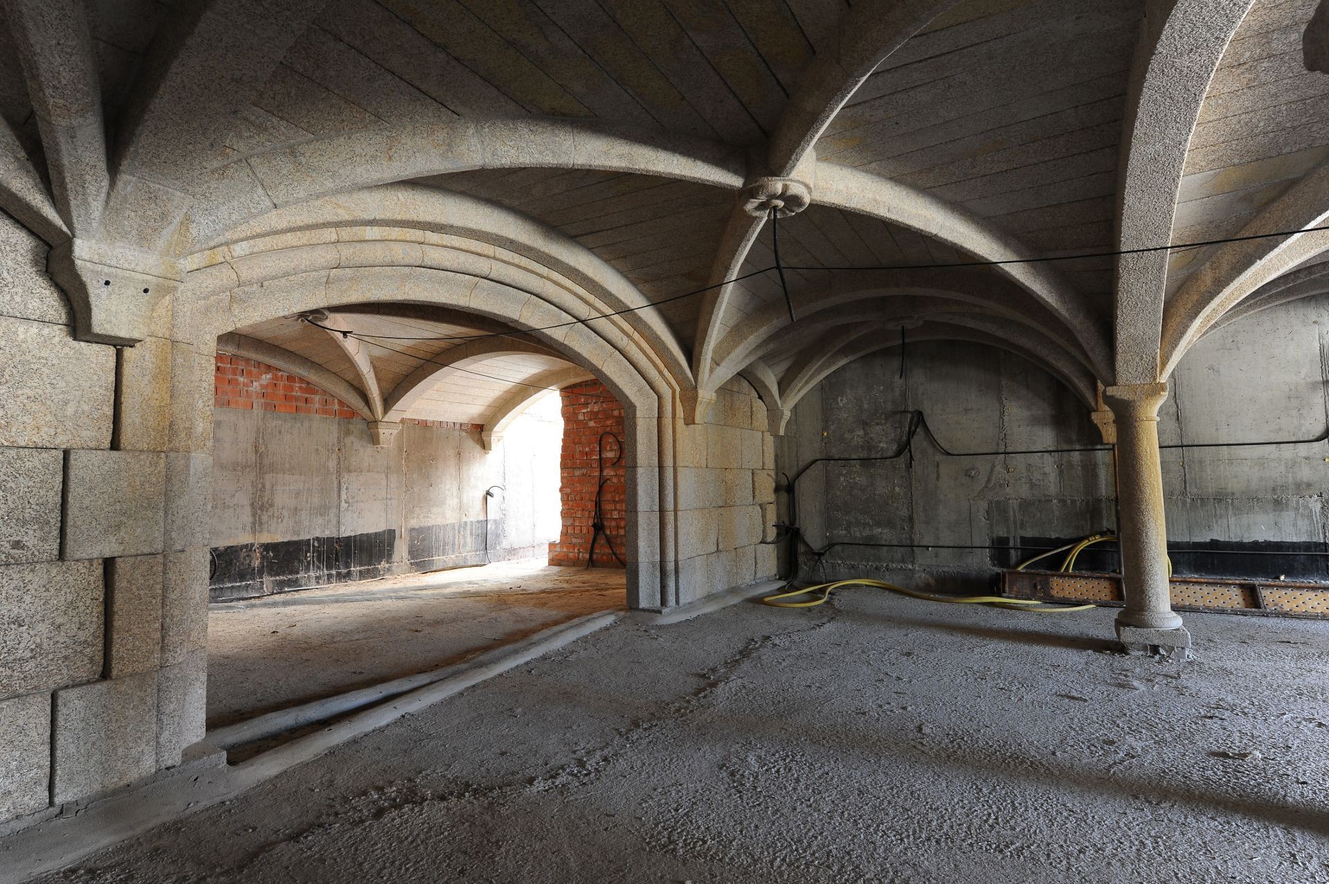 Un interior de piedra con techos abovedados acanalados sostenidos por columnas, con vistas a una abertura luminosa y soleada.